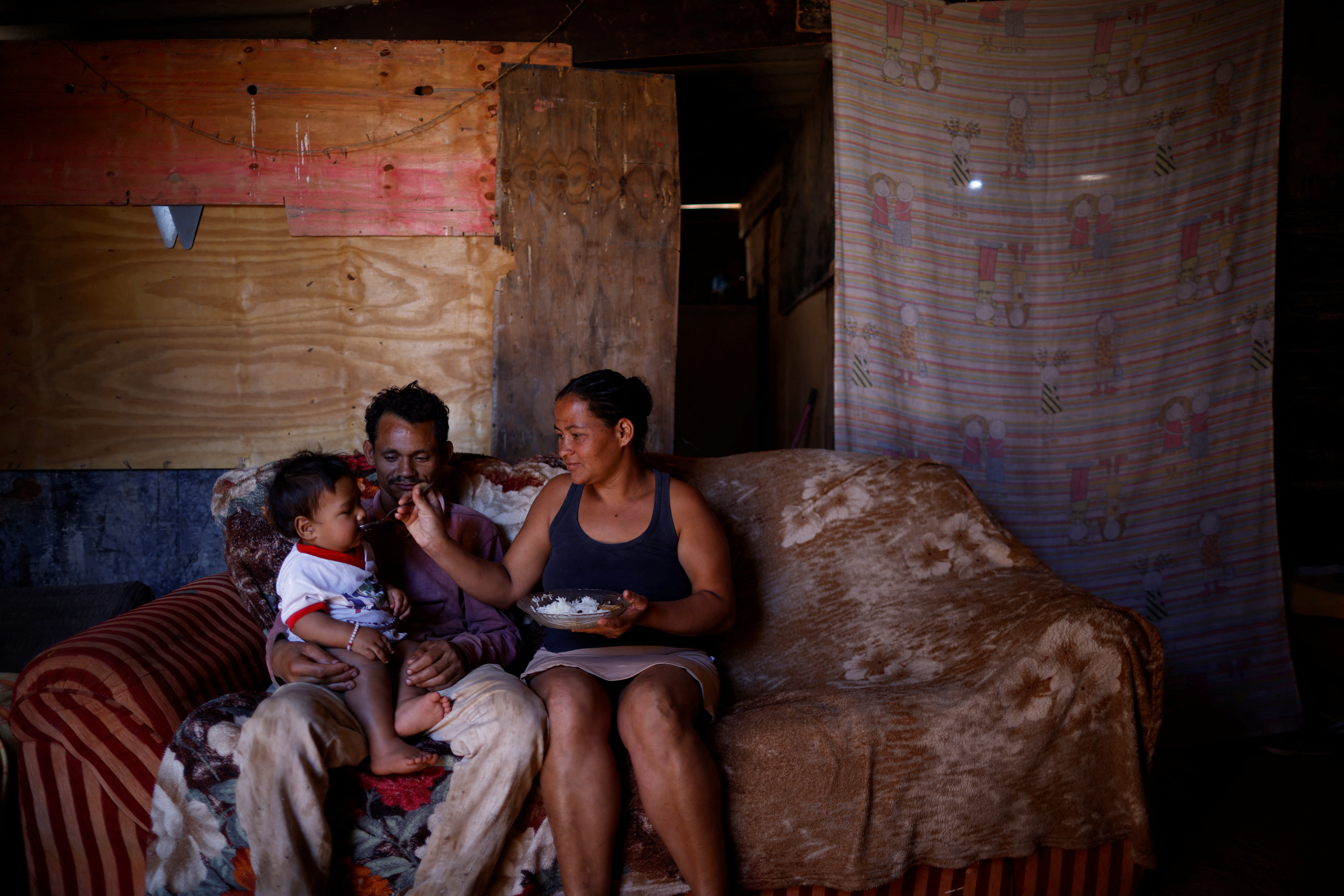 Luciana feeds her 10-month-old baby as he sits on the lap of her husband Felipe dos Santos, 26, at their home