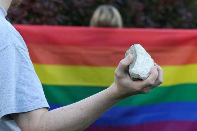 A general view of a person holding a rock behind someone wearing an LGBT pride flag (Jonathan Brady/PA)