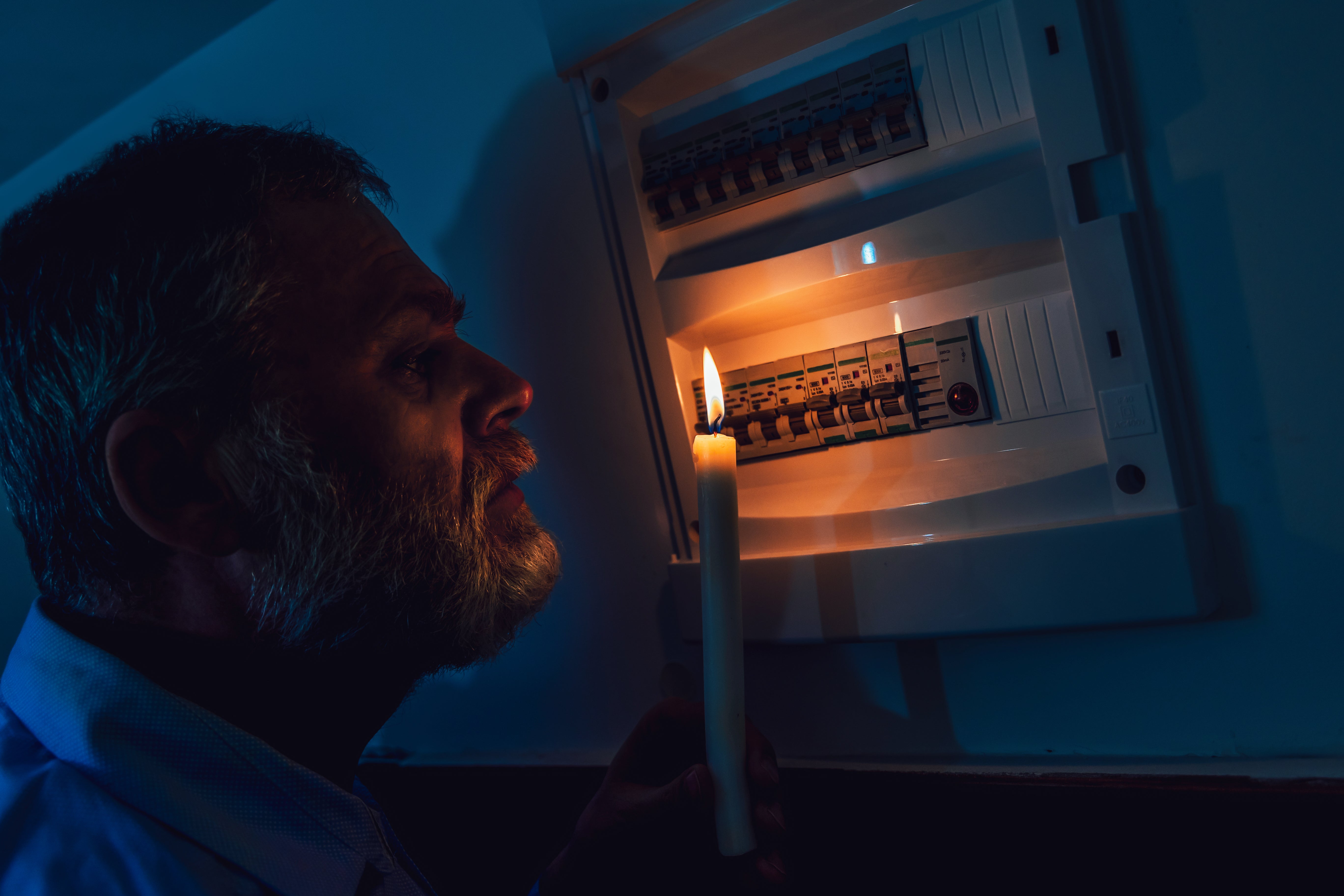 Man in complete darkness holding a candle to investigate a home fuse box during a power outage (stock iamge)