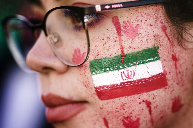 <p>A protester shows red paint in her face, resembling blood splatters and bloody handprints next to the national Iranian emblem</p>