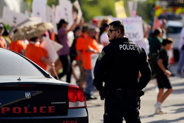 <p>A Uvalde police officer watches as family and friends of those killed and injured in the school shootings at Robb Elementary take part in a protest march and rally, Sunday, 10 July 2022, in Uvalde, Texas</p>