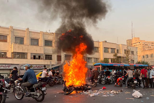 <p>People gather next to a burning motorcycle in the capital Tehran at the weekend</p>