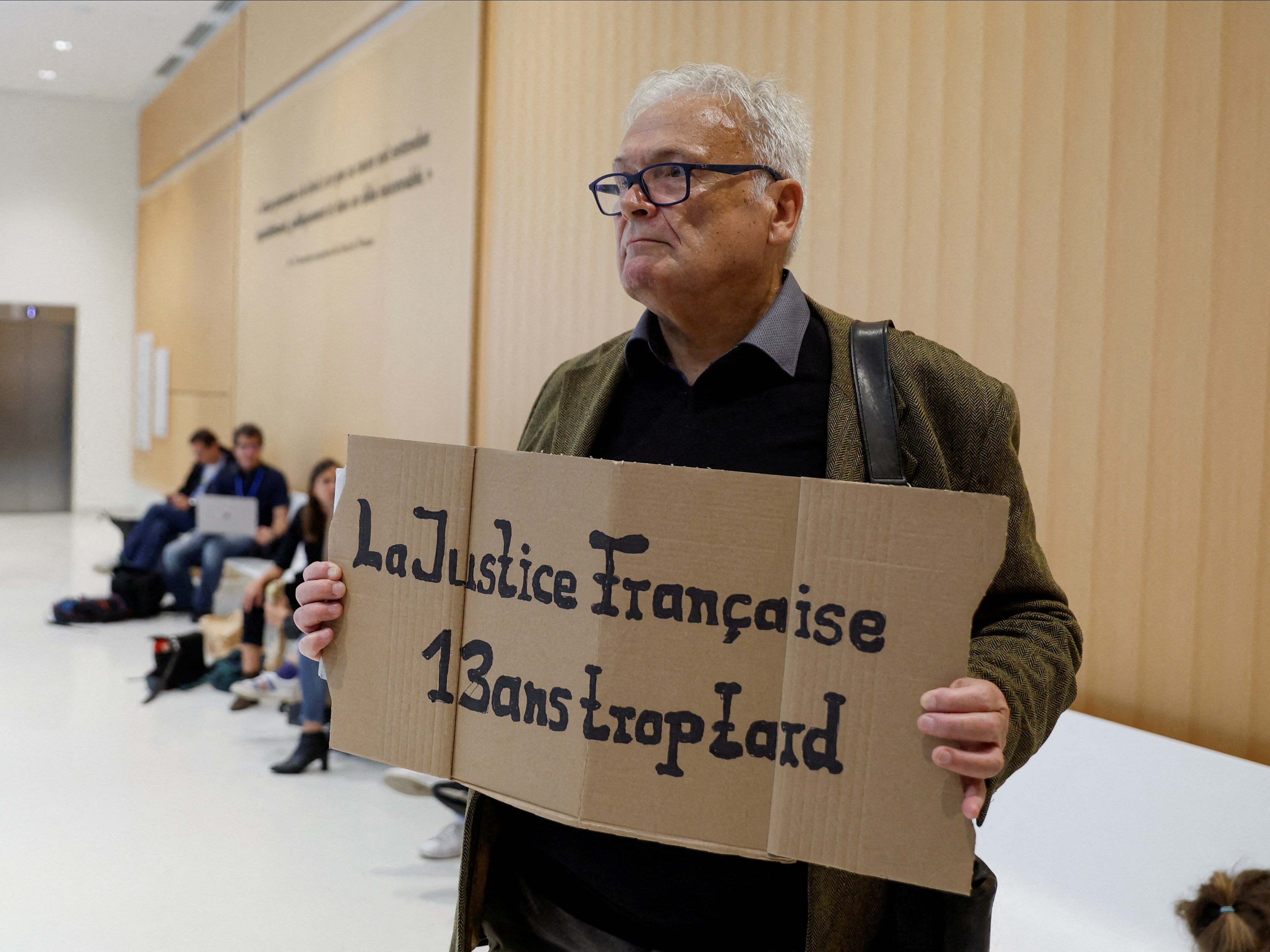 Wilfried Schmid, a family member of a victim, holds a placard that reads ‘French Justice 13 years too late’