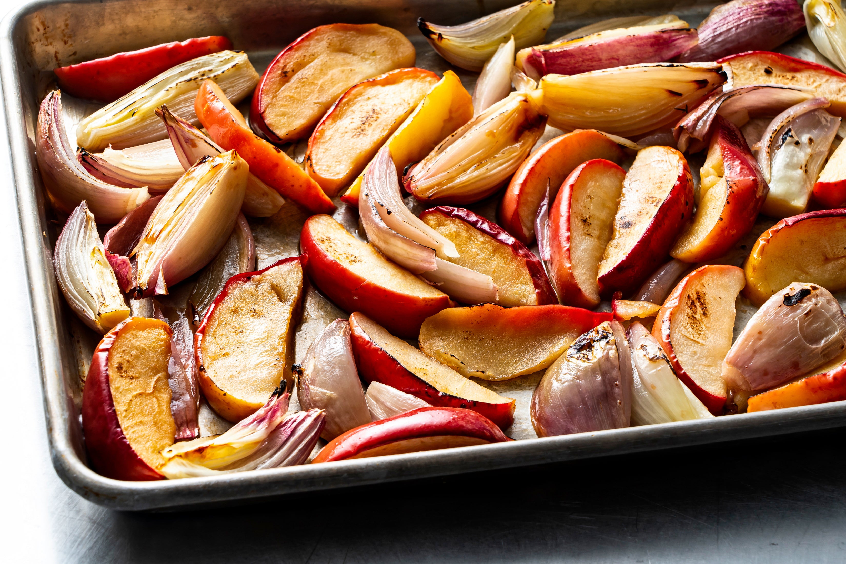 To start, you place wedges of sweet apple and shallot on a sheet pan, toss with a little oil and salt, and cook until they have become soft, sweet and beautifully browned