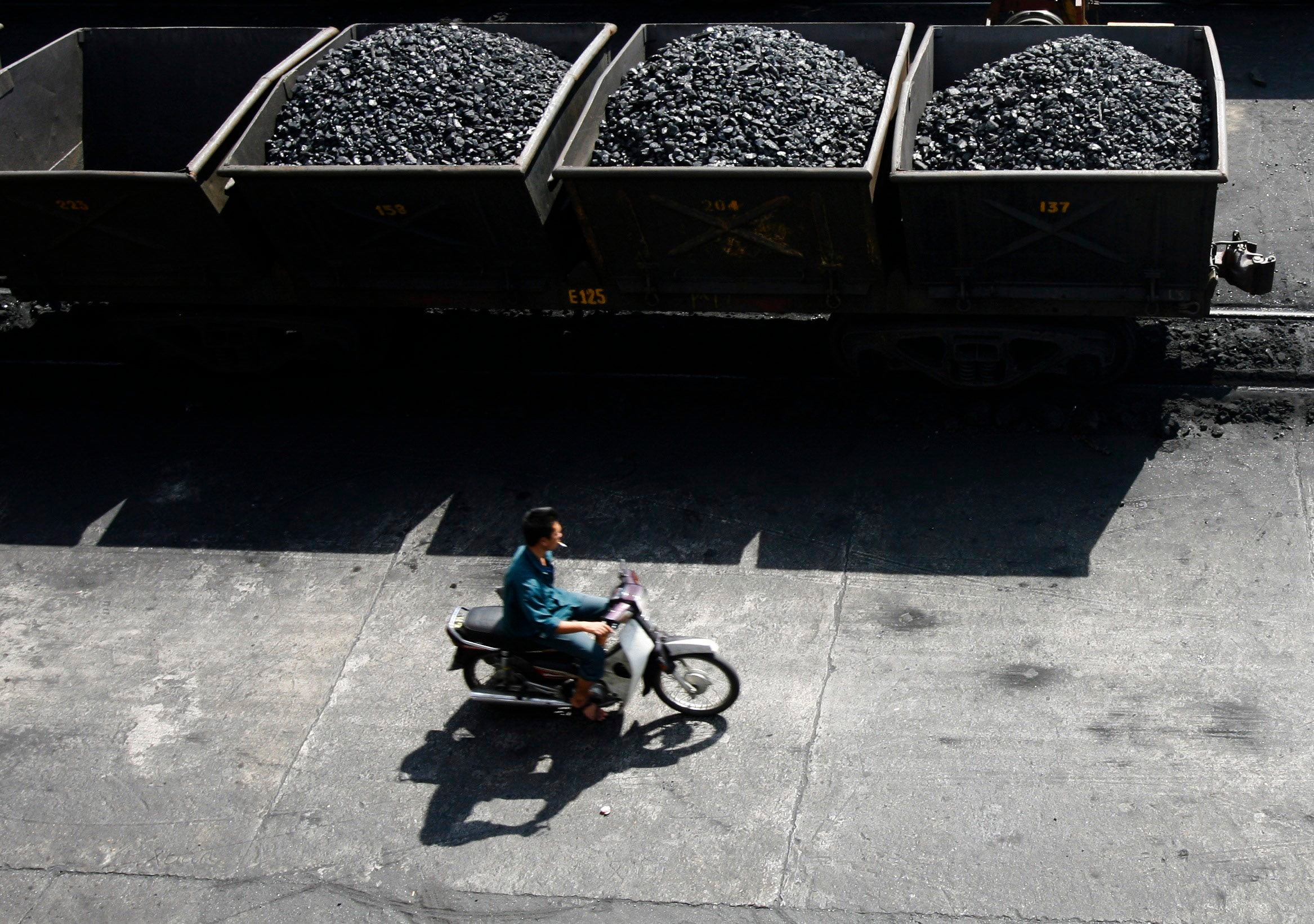 File: A worker rides his motorcycle near lorries transporting coal before it is loaded onto a Chinese ship at a port in Vietnam