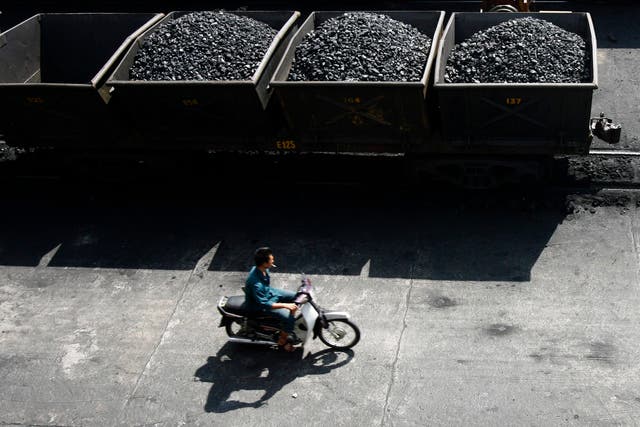 <p>File: A worker rides his motorcycle near lorries transporting coal before it is loaded onto a Chinese ship at a port in Vietnam</p>