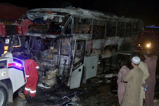 <p>Volunteers gather beside a charred bus on a highway in Nooriabad, Pakistan, Thursday, 13 October 2022</p>