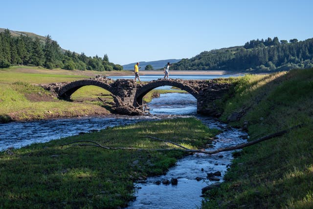 <p>People walk over an exposed bridge that is normally submerged during a heat wave in August in Wales.</p>