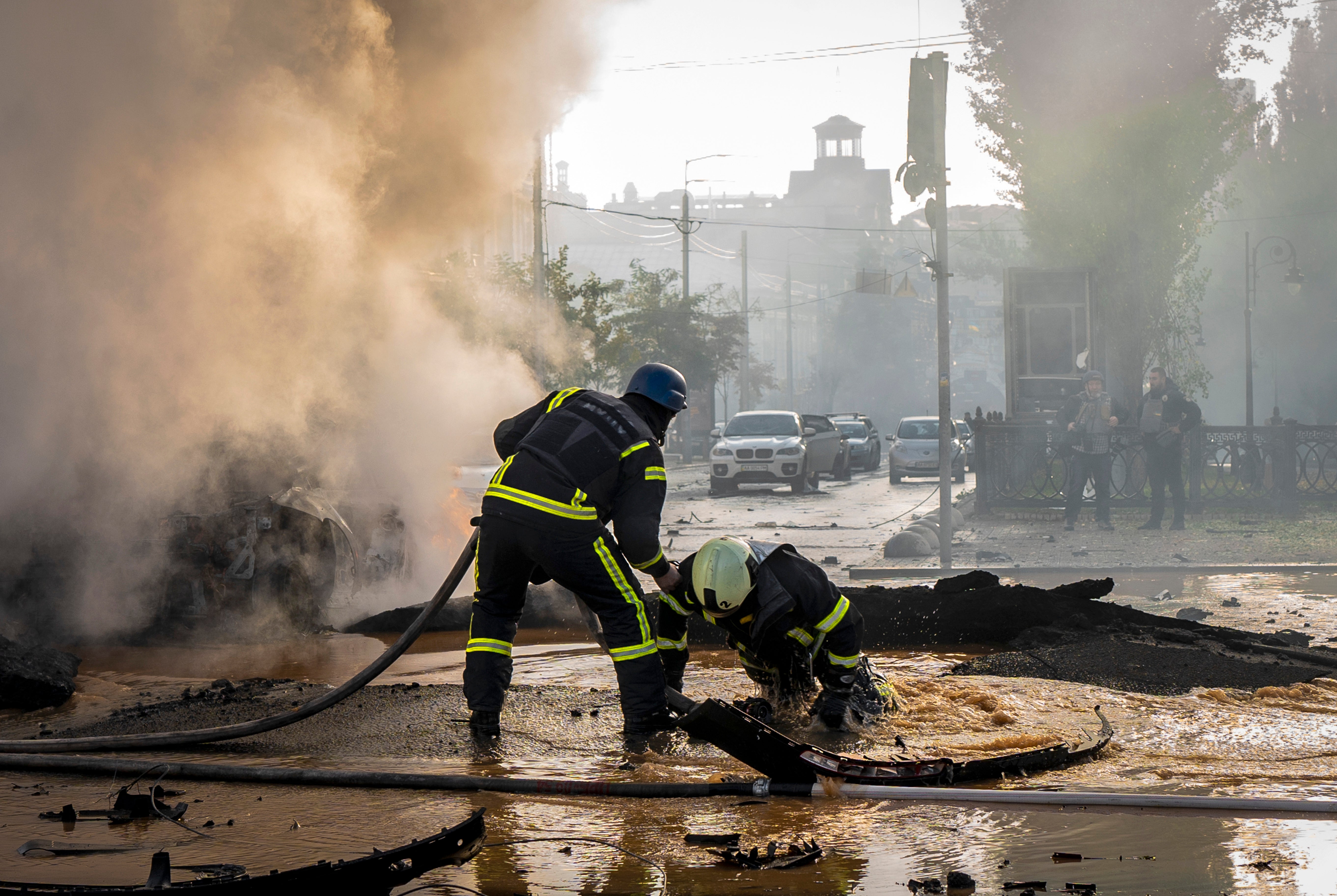 A firefighter helps his colleague to escape from a crater as they extinguish smoke from a burned car after a Russian attack in Kyiv on Monday