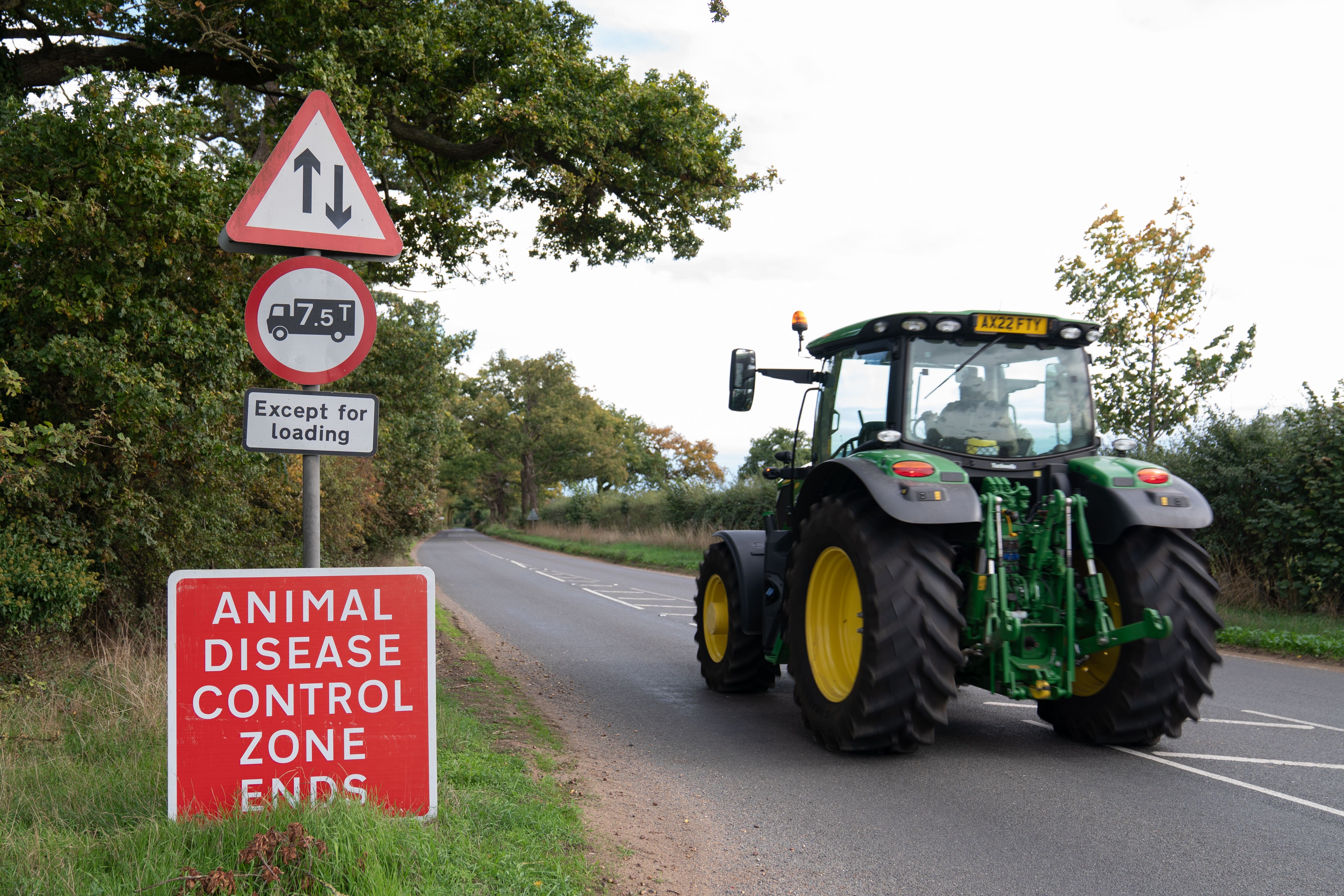 A tractor driving past a sign warning of an animal disease control zone (Joe Giddens/PA)