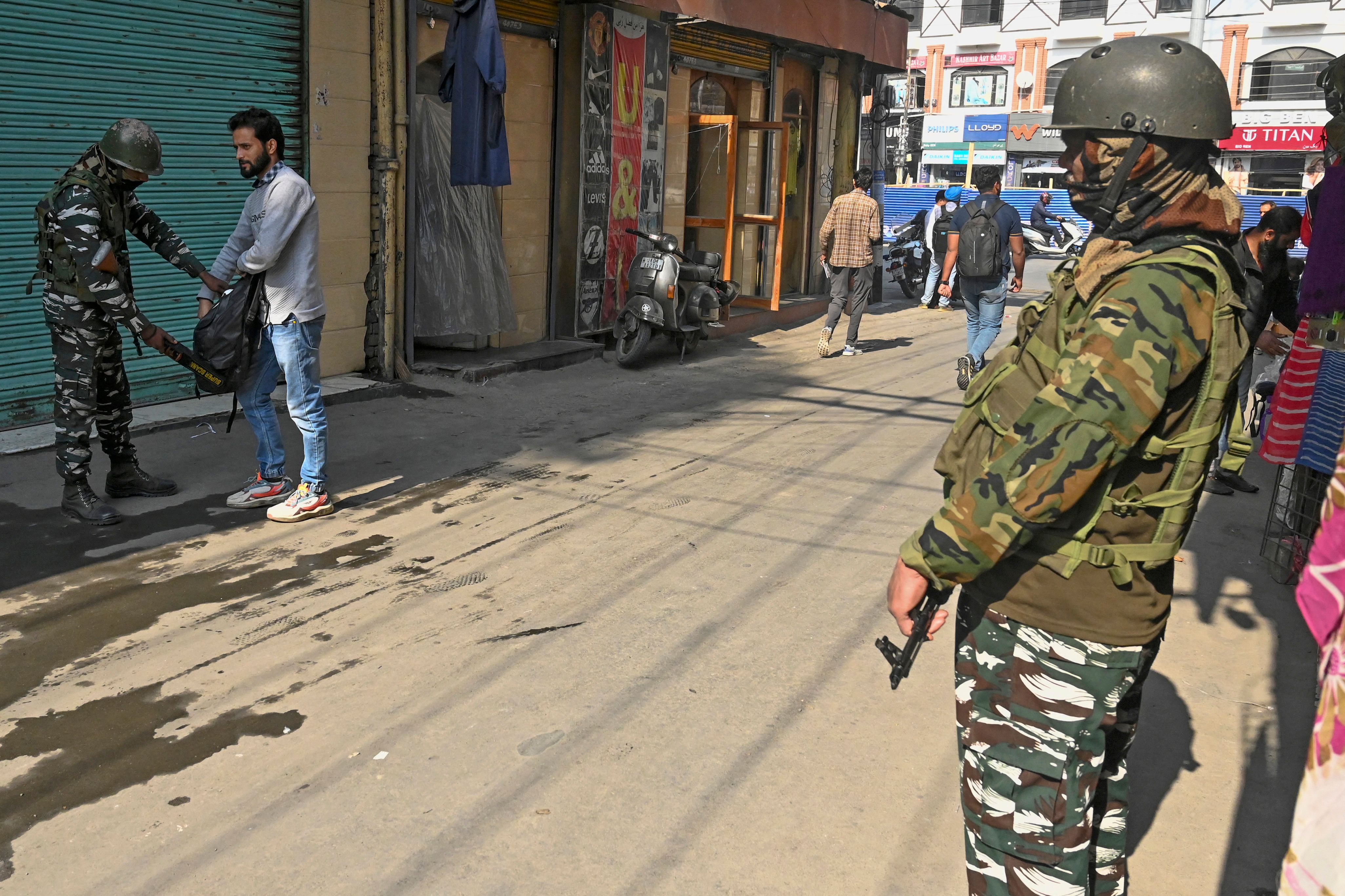 An Indian paramilitary trooper frisks a man’s bag during a random search along a street in Srinagar on 18 October 2022