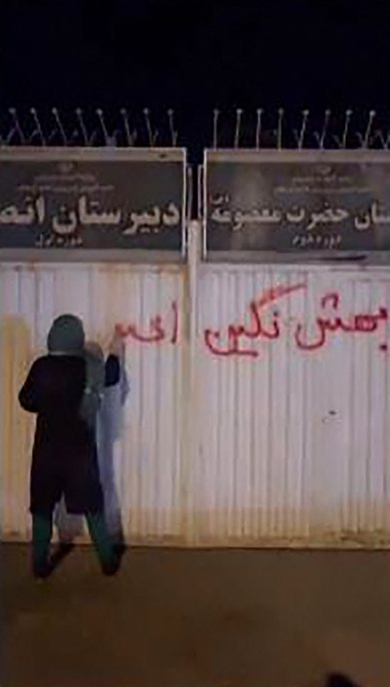 A woman writing graffiti on the wall of a girls' school in the northern Iranian city of Zanjan reading in Farsi: ‘don’t call these protests, this is a revolution’
