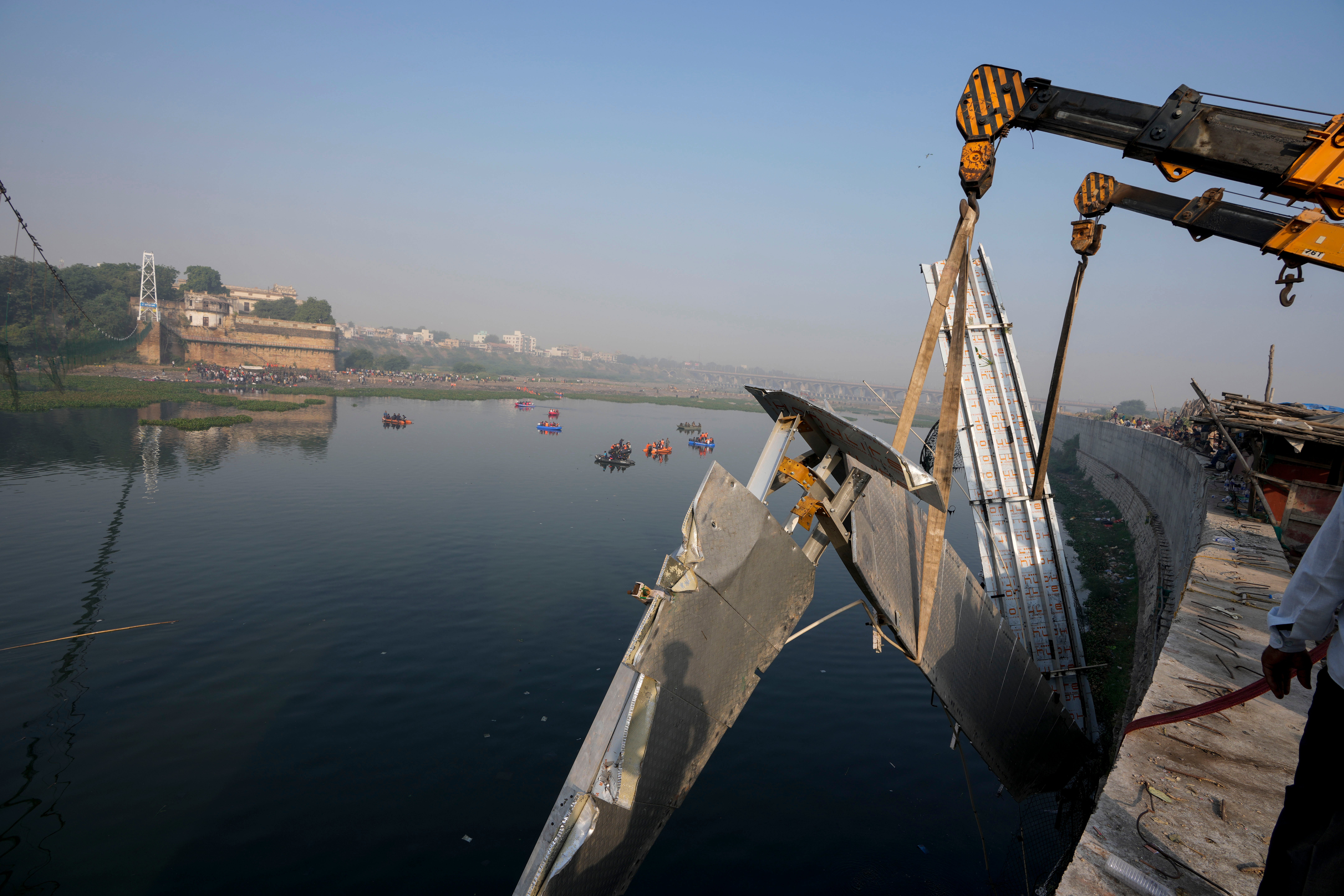 Workers use machinery to remove the debris of a pedestrian bridge that collapsed in Morbi