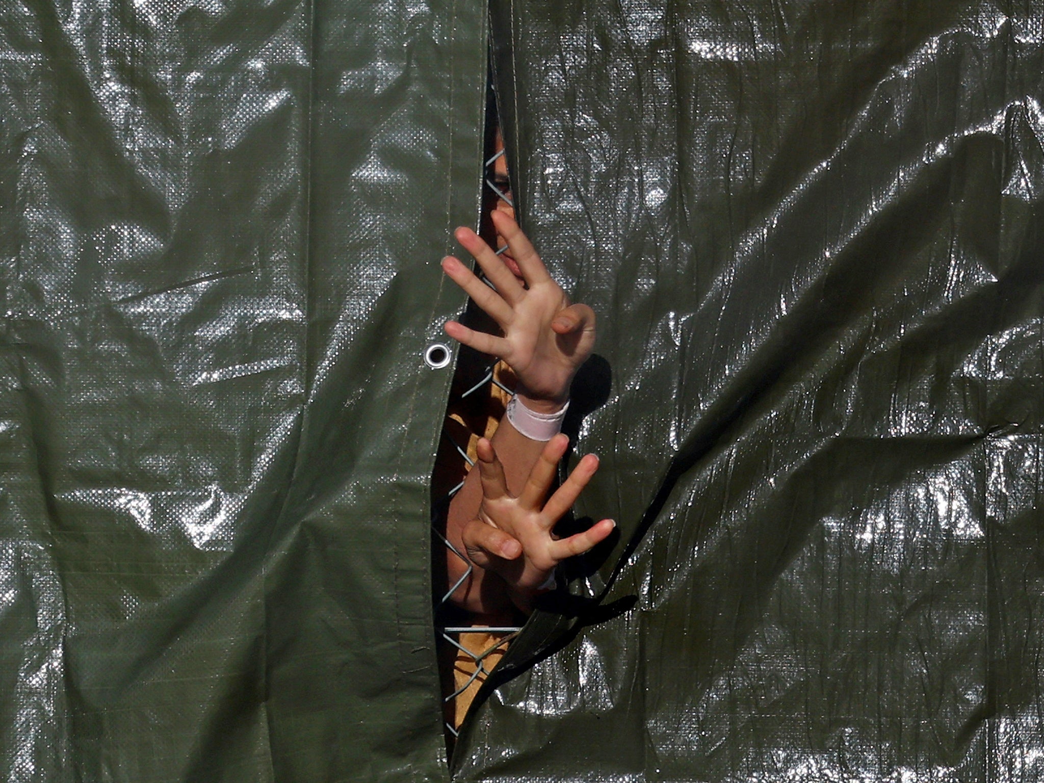 Hands of detainees reach through a fence at Manston