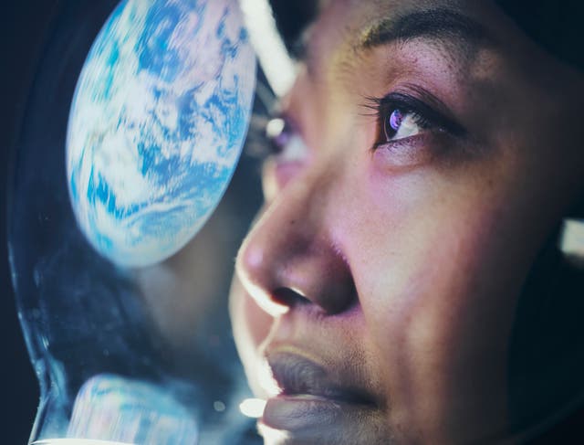 <p>A woman wearing a helmet looking at Earth from space. (Earth image provided by NASA)</p>