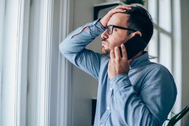 <p>Worried businessman with hand on forehead talking on mobile phone in his office.</p>