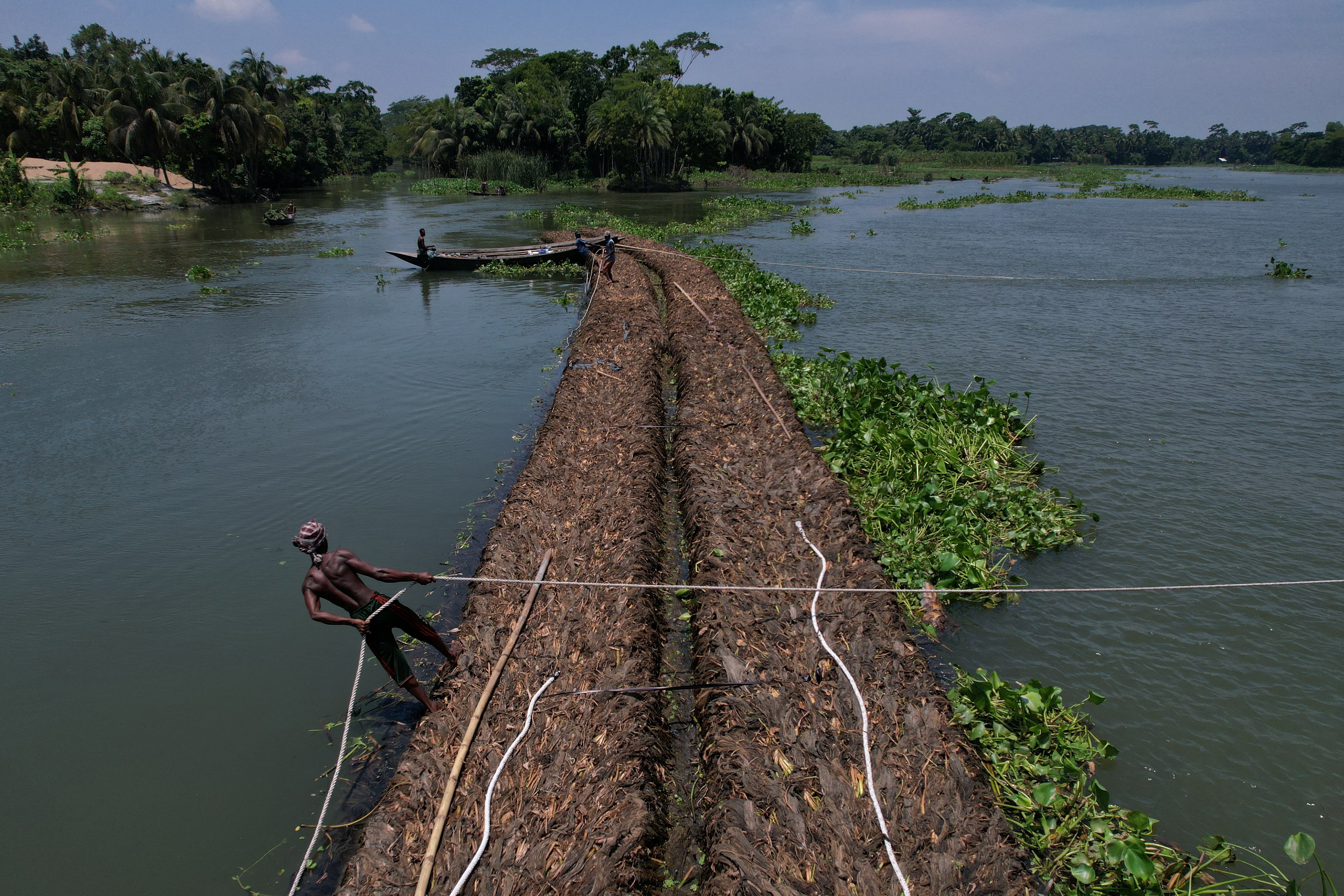 A man holds a rope as people transport floating beds towards a farm through the Belua river