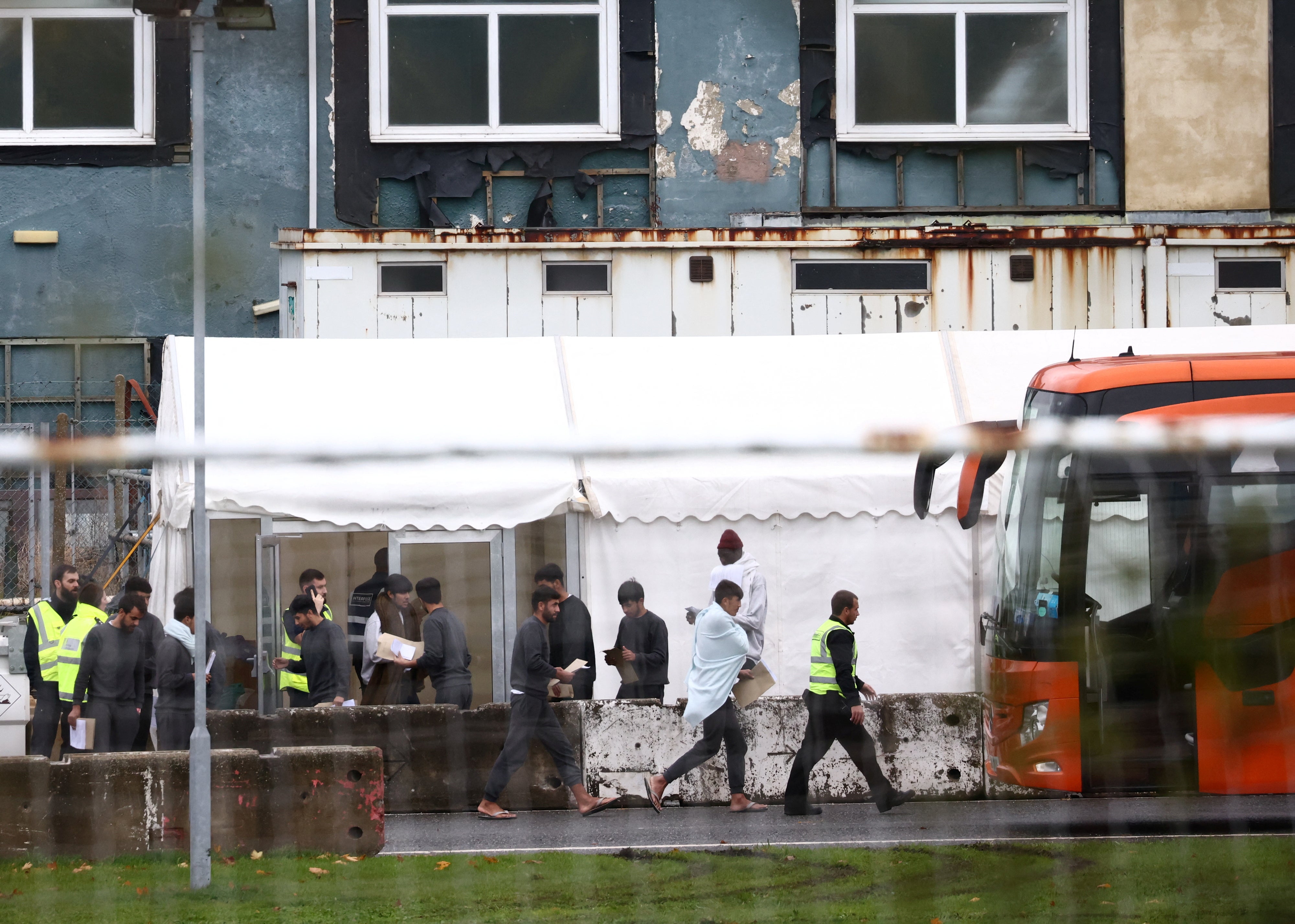 People board a bus inside the migrant processing centre, during the visit of Suella Braverman, in Manston