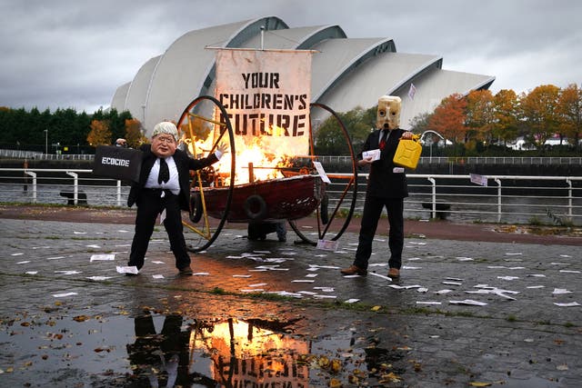 Performers from Ocean Rebellion dressed as Prime Minister Boris Johnson and an Oilhead set light to the sail of a small boat which reads “Your Children’s Future” as they burn stacks of money on the banks of the River Clyde in Glasgowm close to the site of the upcoming Cop26 conference, highlighting the degradation of the Ocean. The scene represents what rotesters have said is “the UK government’s total lack of purpose in combating catastrophic climate change.” Picture date: Wednesday October 27, 2021. (Andrew Milligan/PA)