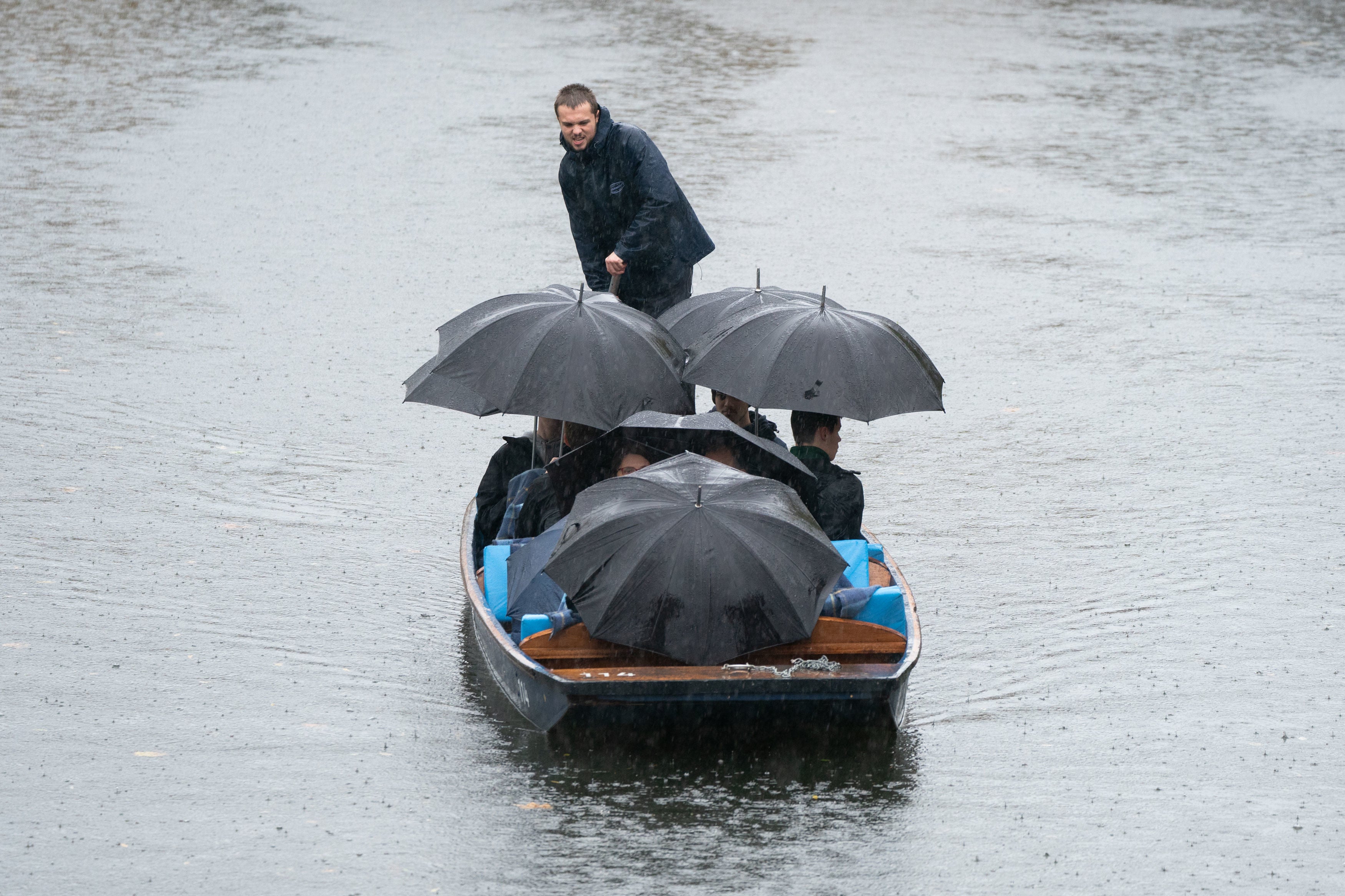 People shelter under umbrellas as they punt along the River Cam in Cambridge during a heavy rain shower