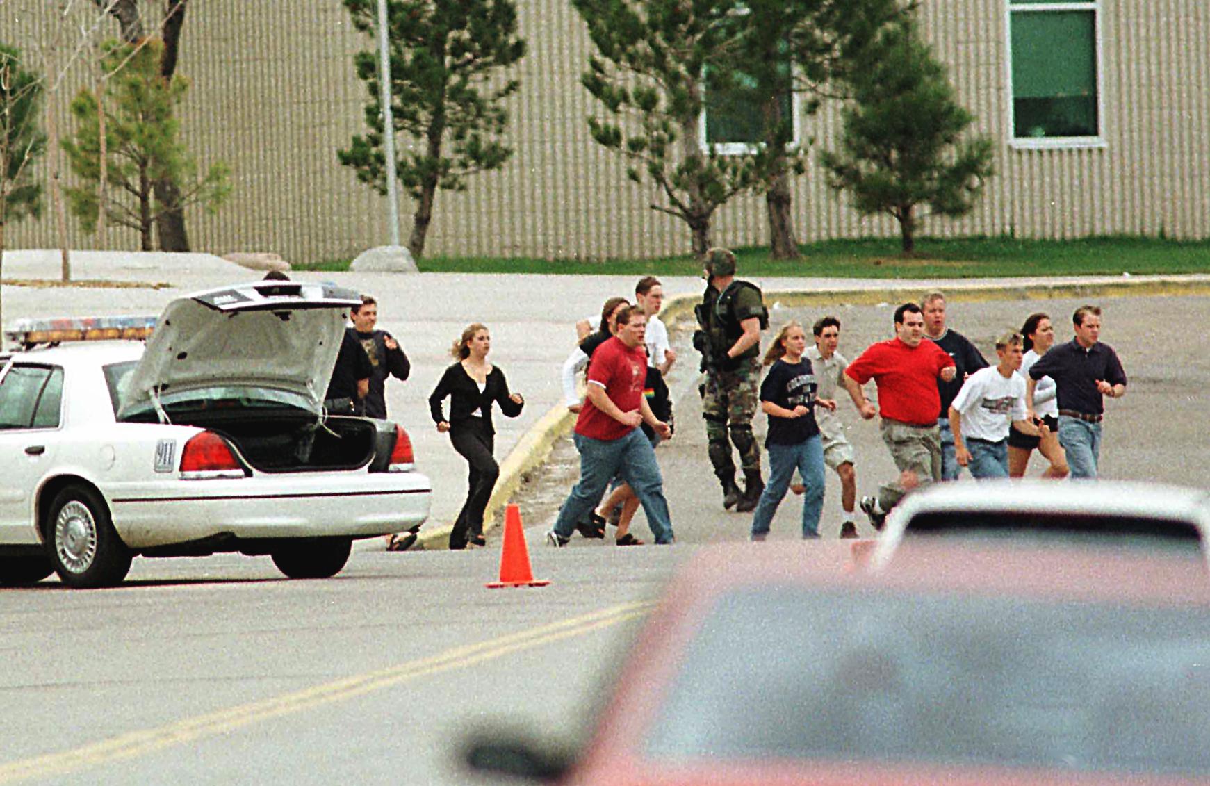 Students run from Columbine High School run under cover from police 20 April 1999 in Littleton, Colorado