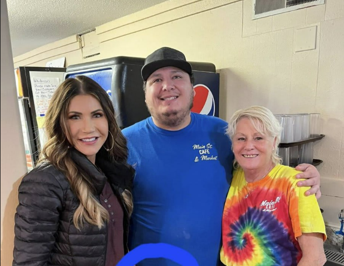 <p>Stefen Monteau (centre) was pulled into a picture alongside Kristi Noem (left), the incumbent Republican running in South Dakota’s gubernatorial race on 8 November</p>