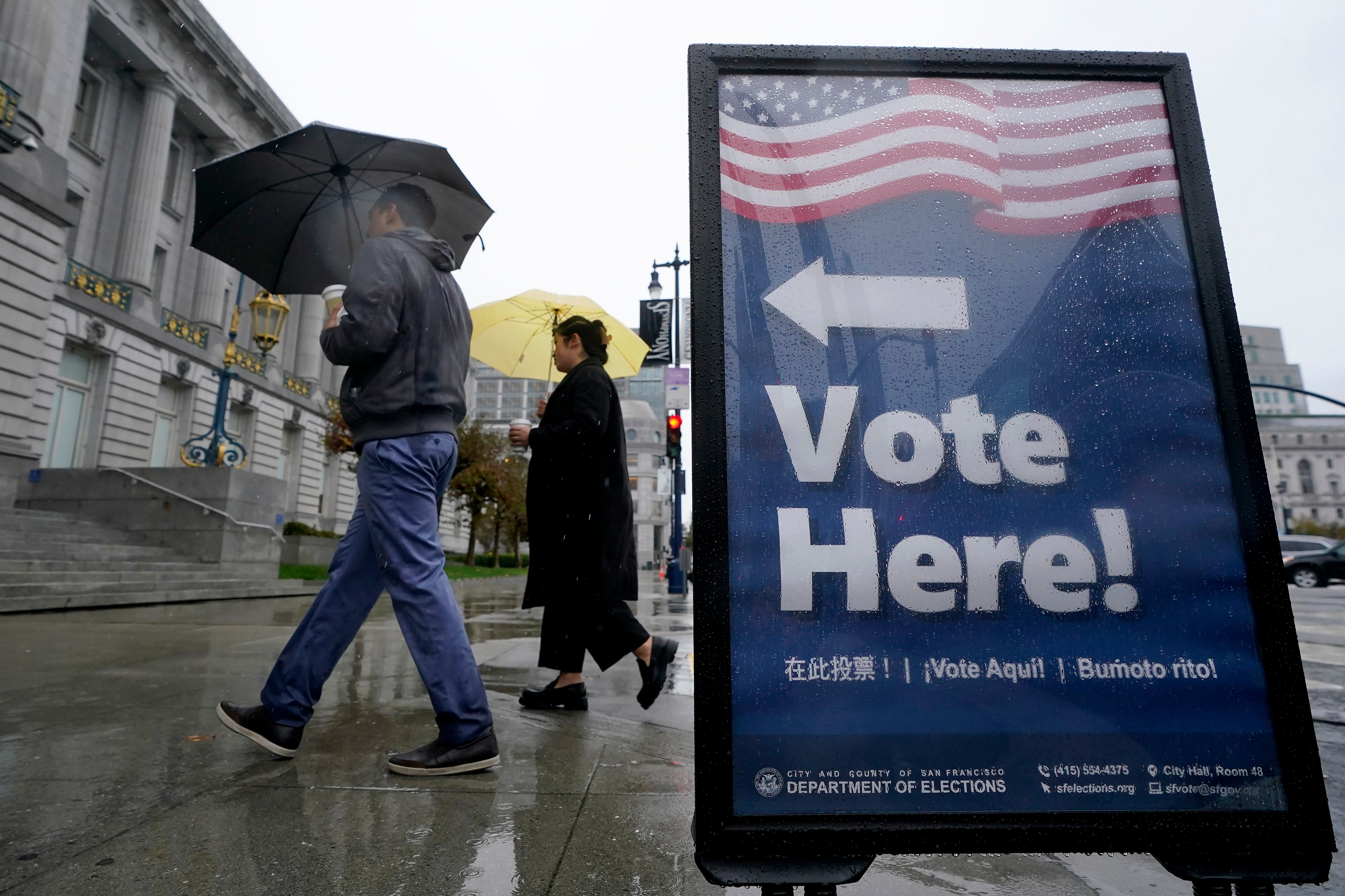 People carry umbrellas while walking past a voting sign outside City Hall in San Francisco
