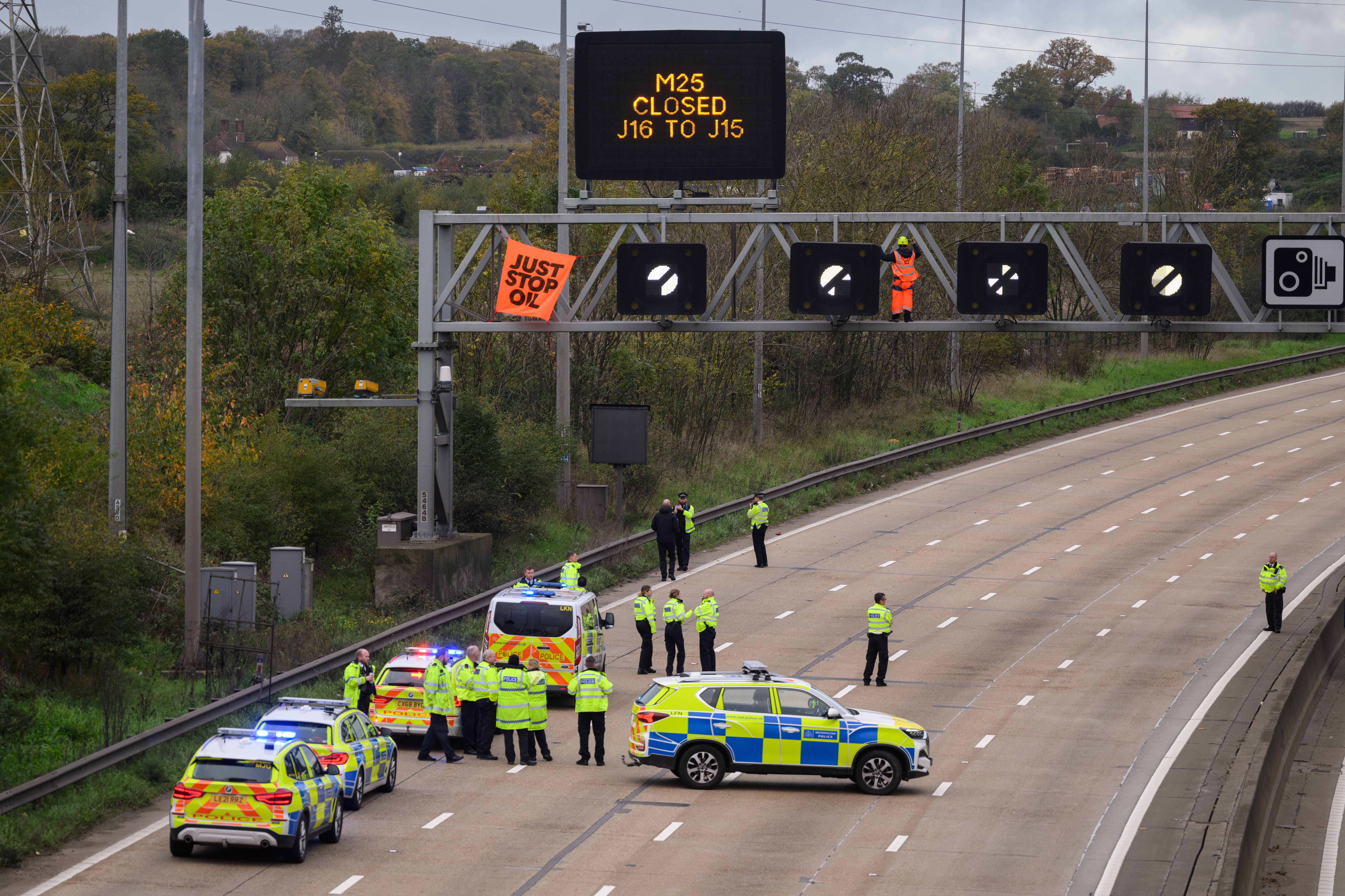 <p>Police officers block the highway as an activist puts up a banner on a gantry on the M25</p>