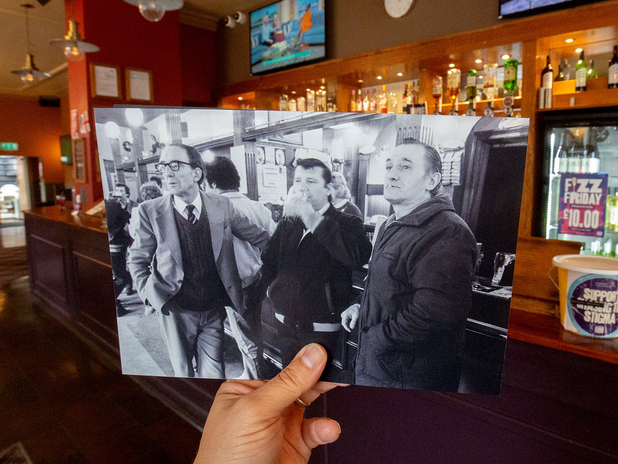 Harry Atkinson, Arthur ‘Arty’ Lee and Ray ‘Scadge’ Hardy watching the racing in the Star & Garter in Hull, 1983 held up against the same pub in 2022