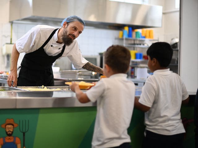 <p>A school chef serves cooked hot dinner to students on their lunch break at St Luke’s Church of England Primary School in east London</p>