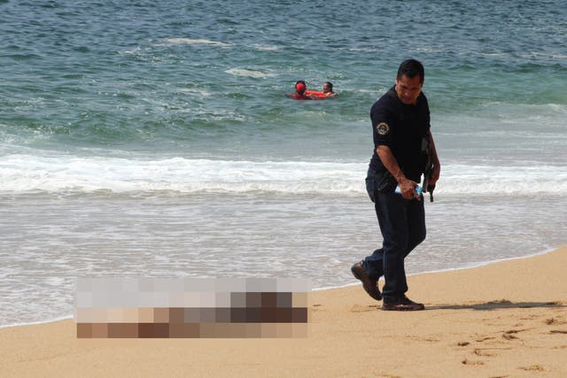 <p>MATERIAL SENSIBLE. ESTA IMAGEN PUEDE OFENDER O MOLESTAR Un policía camina cerca de uno de los tres cuerpos con signos de tortura que han sido arrastrados por el mar, según medios locales, en la playa Icacos, en</p>
