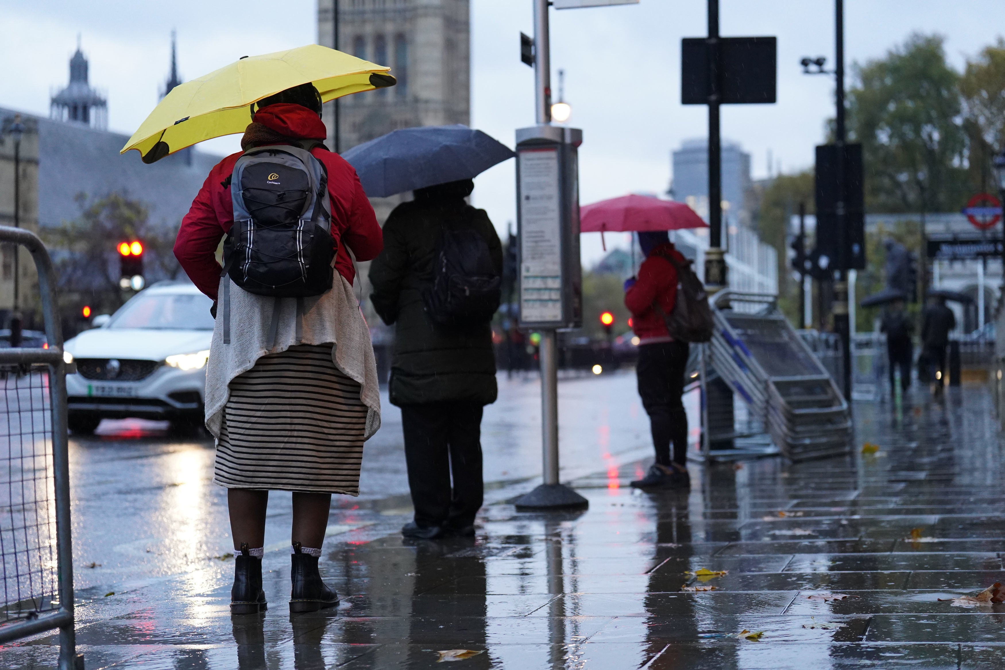 People hold umbrellas as they wait in the rain at a bus stop in Whitehall, London