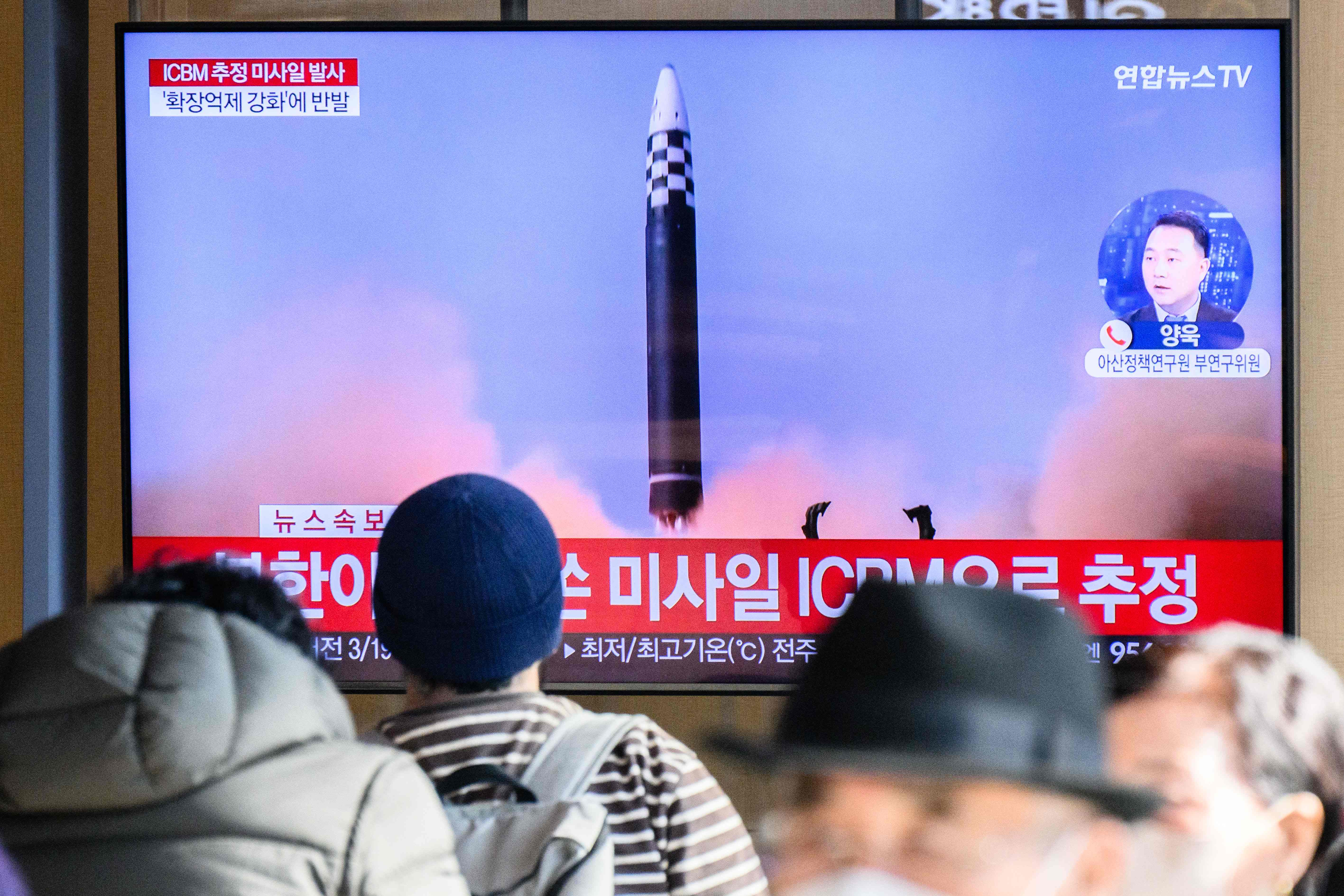 People sit near a television showing a news broadcast with file footage of a North Korean missile test, at a railway station in Seoul