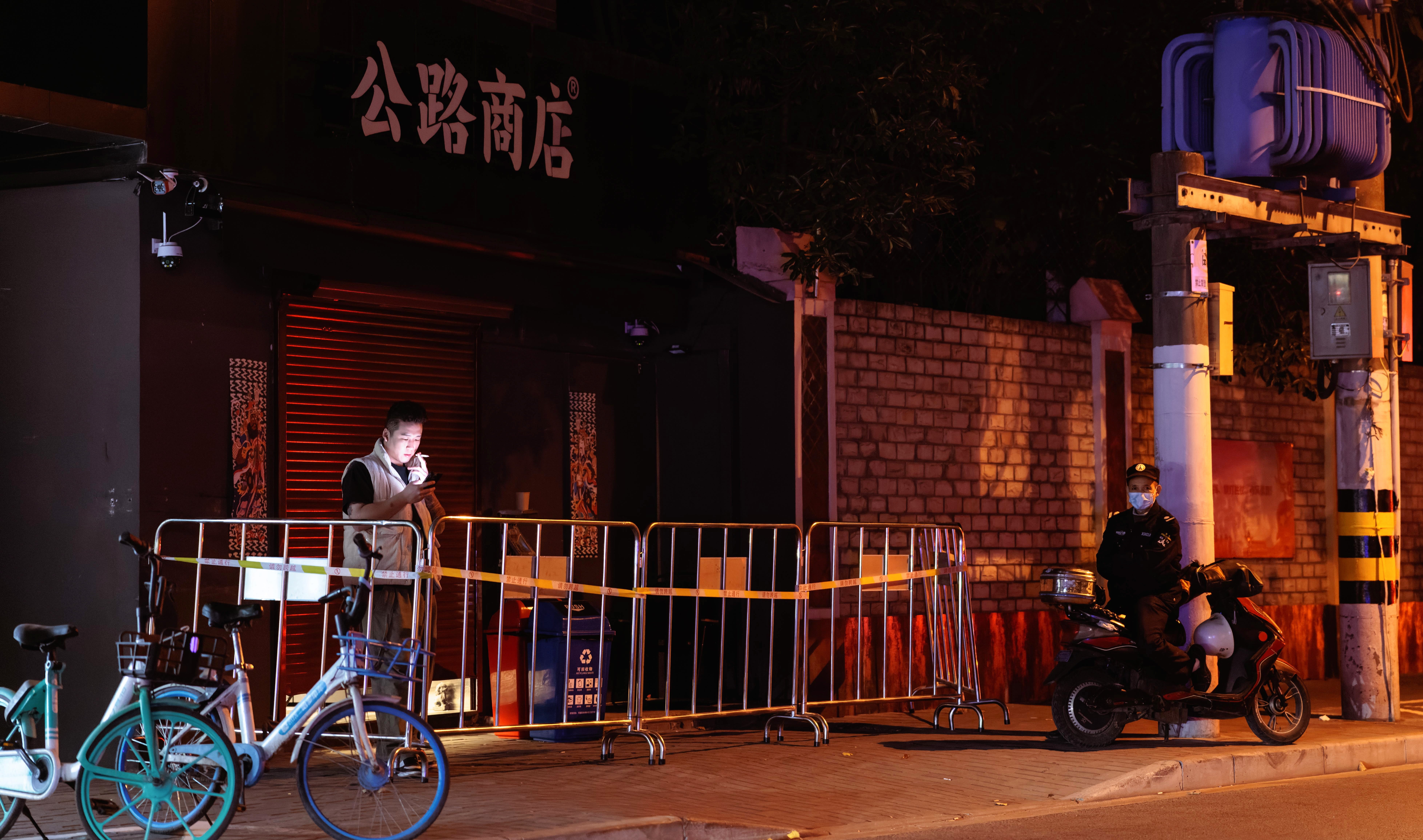 <p>A man uses his phone in area under quarantine as a security guard looks on, in Shanghai</p>