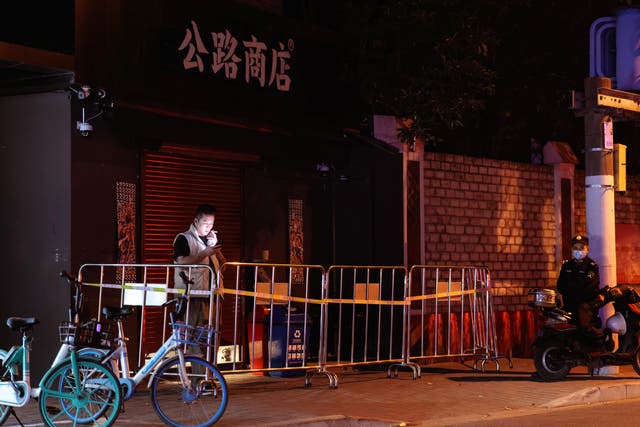 <p>A man uses his phone in area under quarantine as a security guard looks on, in Shanghai</p>
