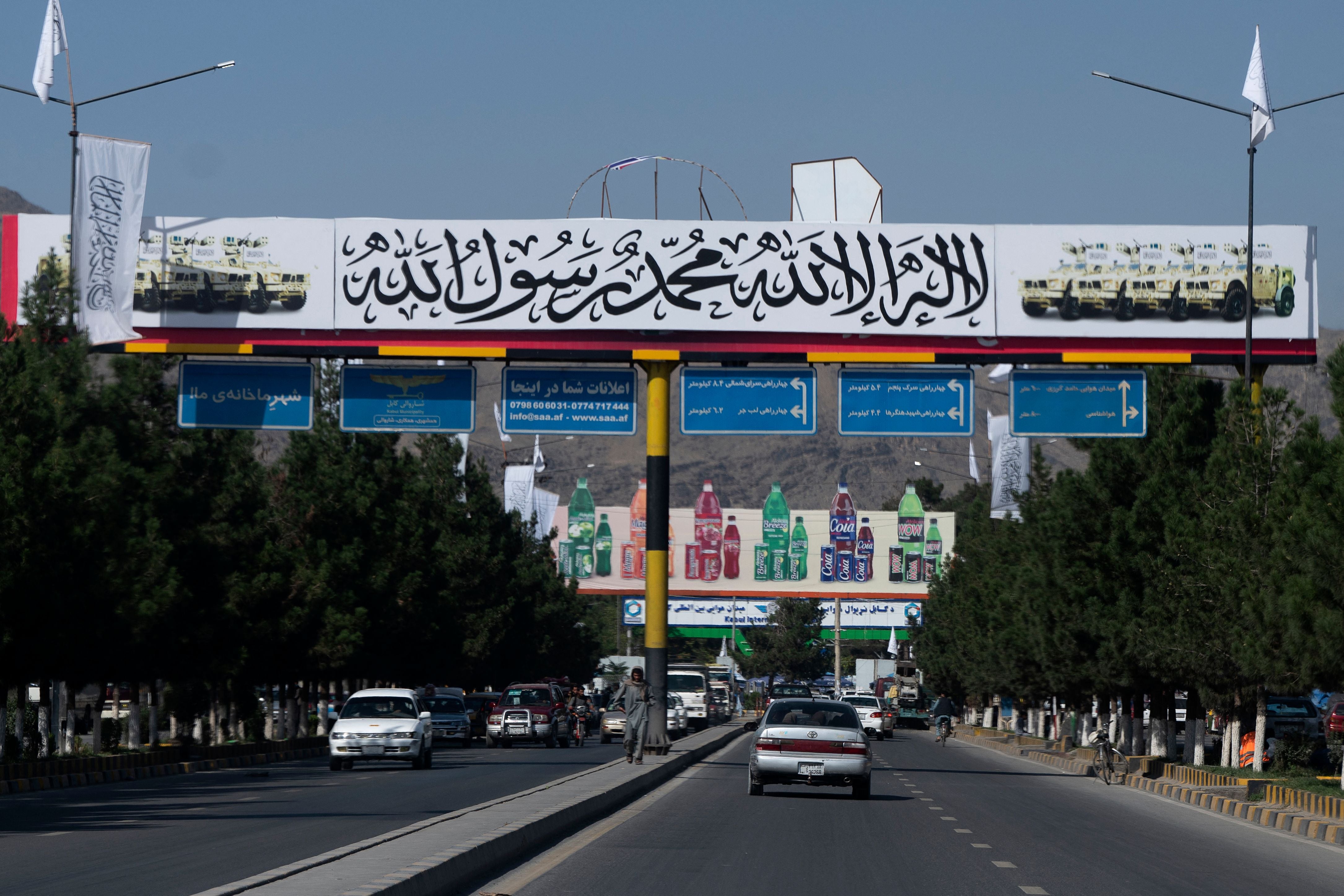 Commuters make their way under a banner placed by Taliban authorities near Kabul airport