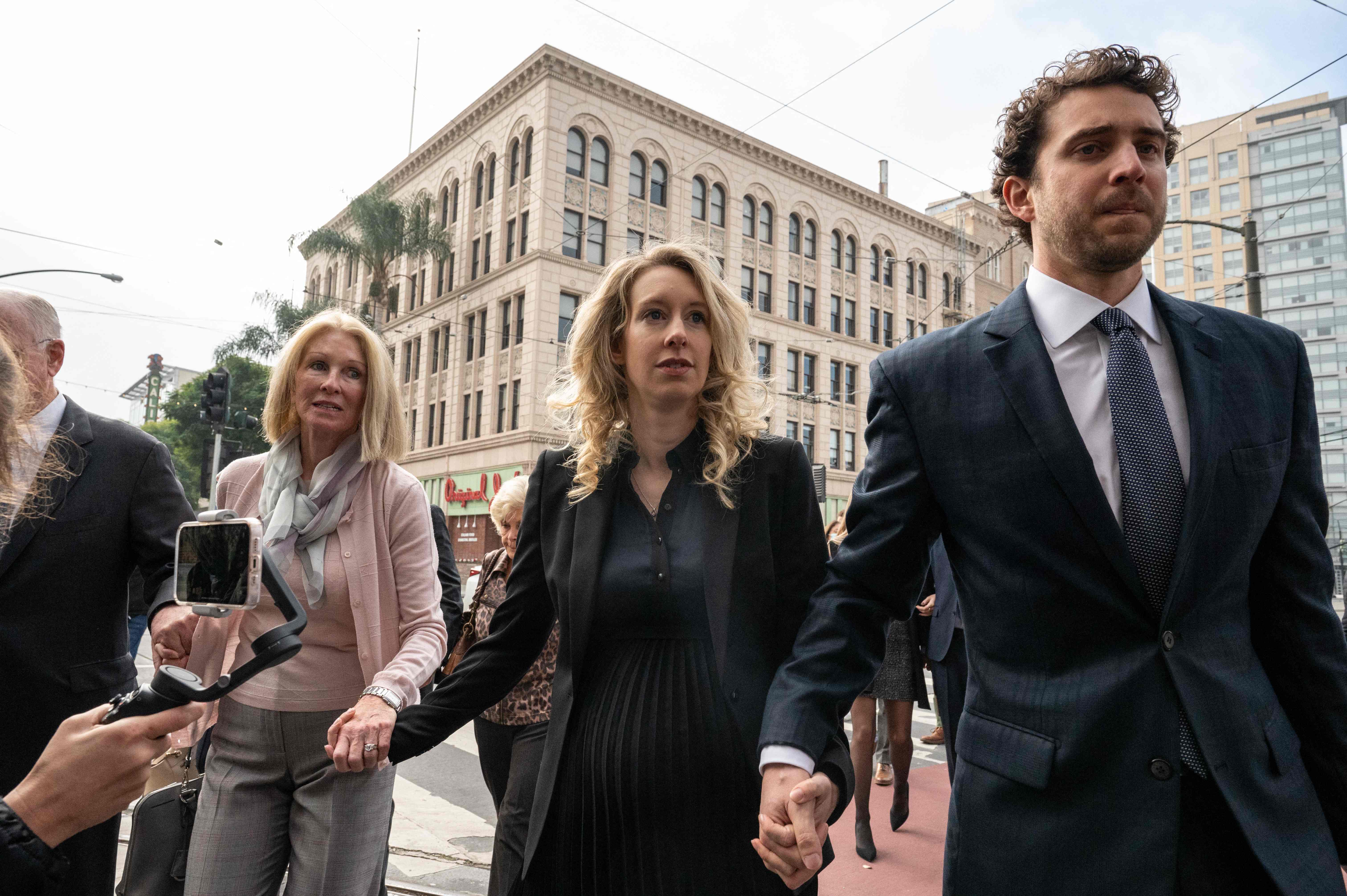 Elizabeth Holmes (C), founder and former CEO of blood testing and life sciences company Theranos, walks with her mother Noel Holmes and partner Billy Evans into the federal courthouse for her sentencing