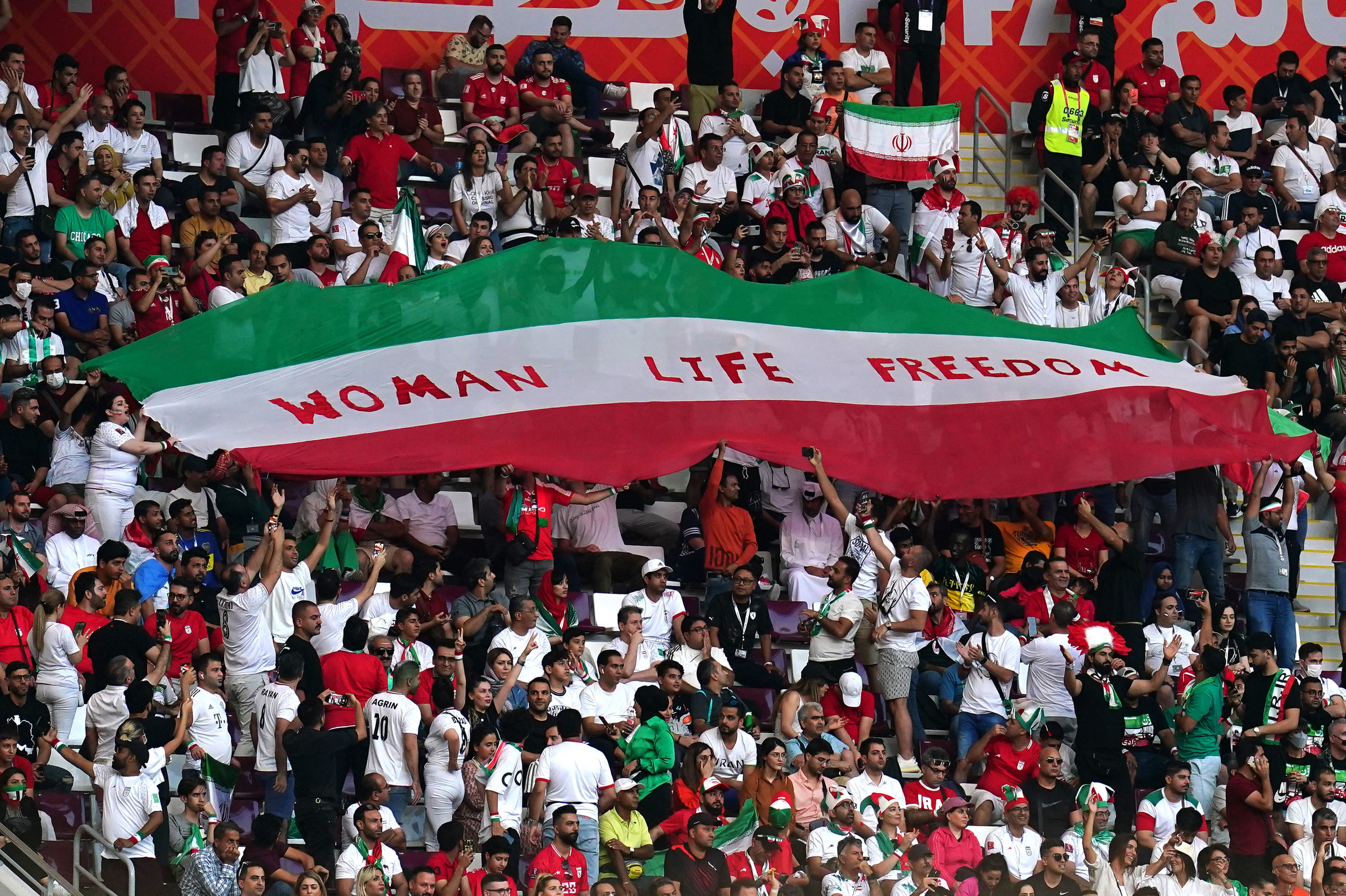 Iran fans in the stands hold up an Iran flag reading "Woman Life Freedom"