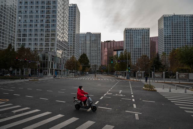 <p>A woman drives a scooter across a nearly empty intersection in the Central Business District, after many offices were closed or workers expected to work from home to prevent the spread of Covid-19 in Beijing, China.</p>