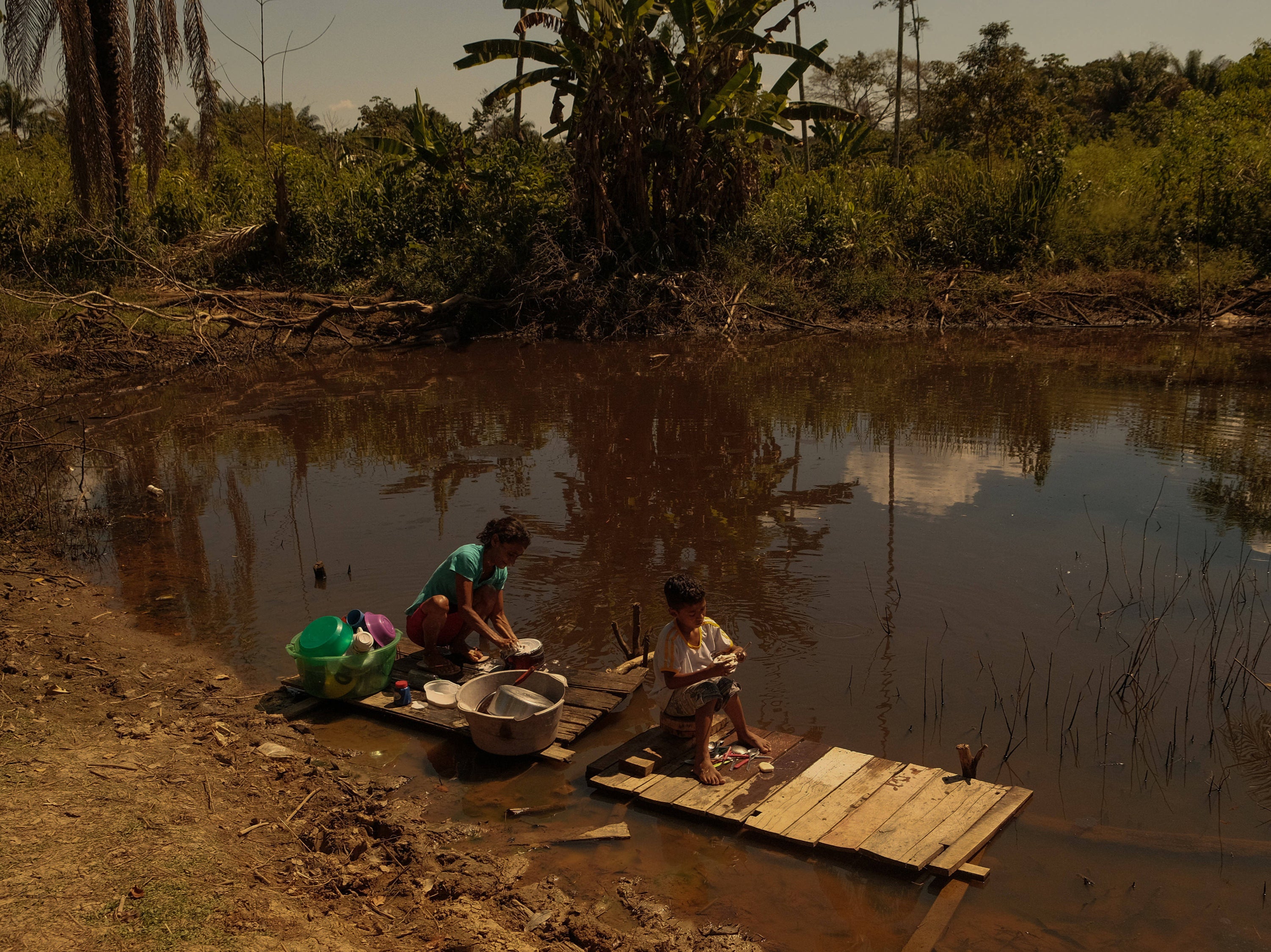 Antonia Franco dos Santos and her grandson wash dishes in a nearby pond