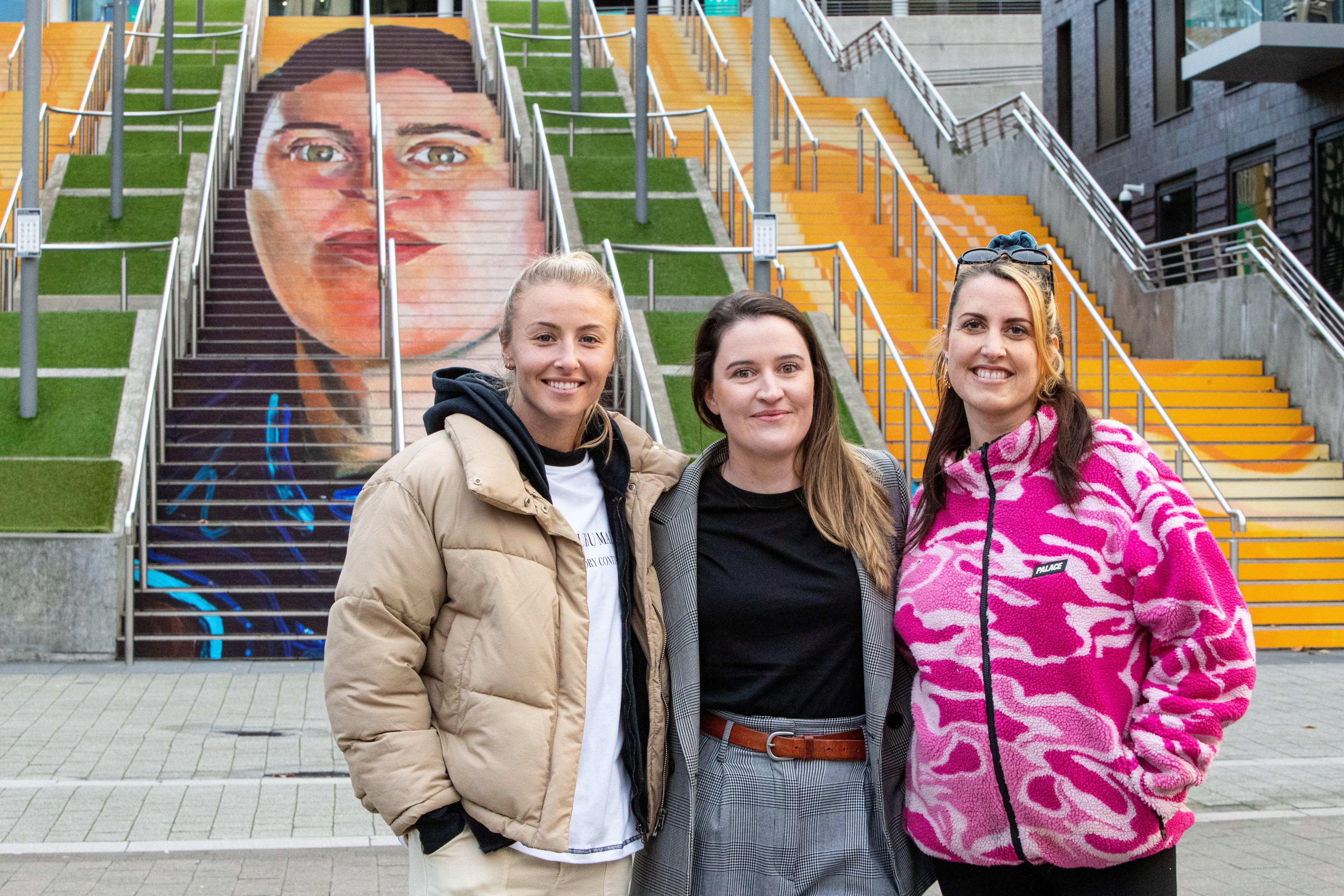 Leah Williamson unveils a mural by artist Charlotte Archer (right) on the Spanish Steps of Wembley Stadium, which depicts Helen Hardy (centre) founder of Manchester Laces