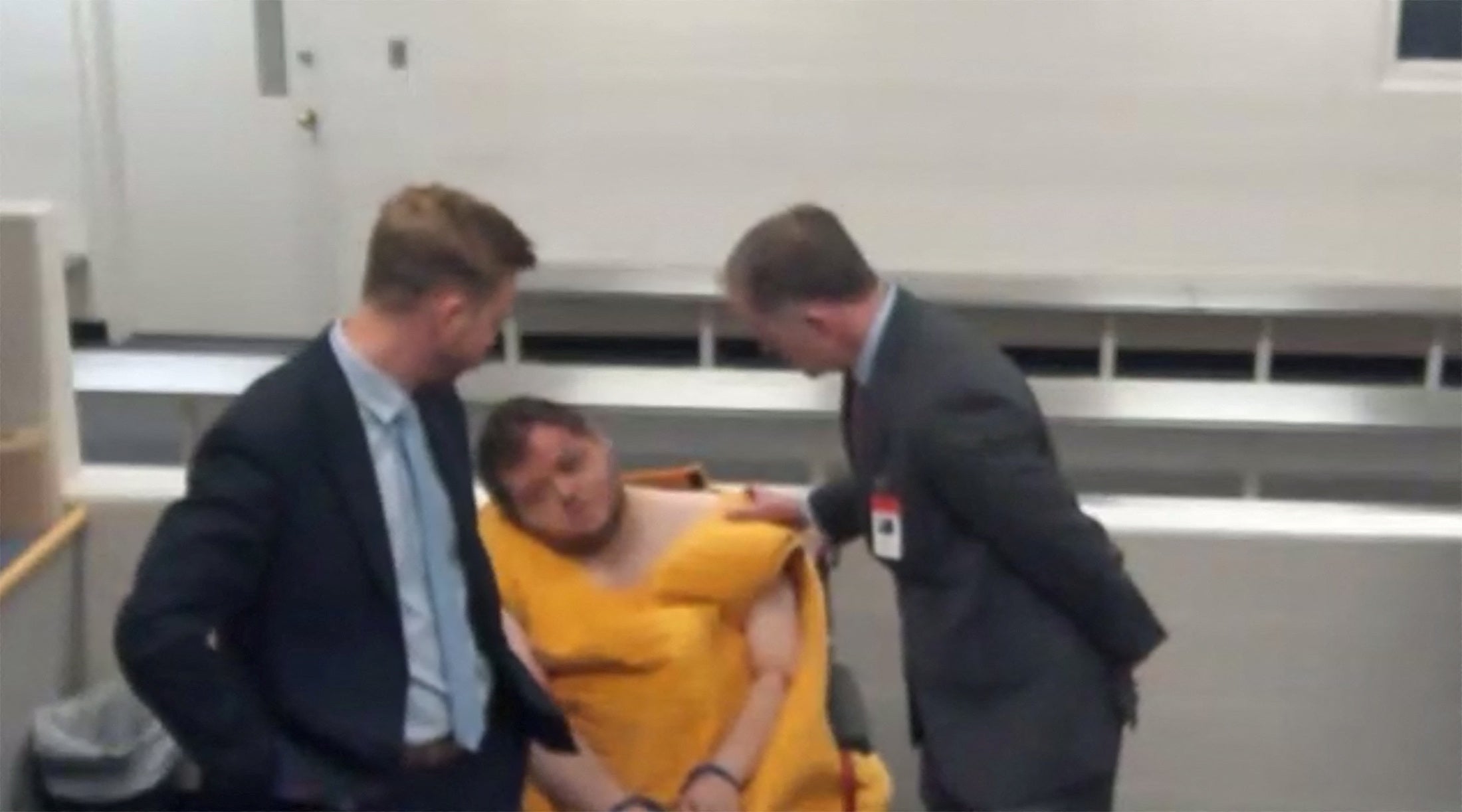 Anderson Lee Aldrich, 22, the suspect in the mass shooting that killed five people and wounded 17 at an LGBTQ nightclub appears with state public defenders Joseph Archambault and Michael Bowman before a judge during their advisement hearing in a video link from jail, slumped to the side and in a wheelchair and showing facial injuries in a still image from video in Colorado Springs, Colorado
