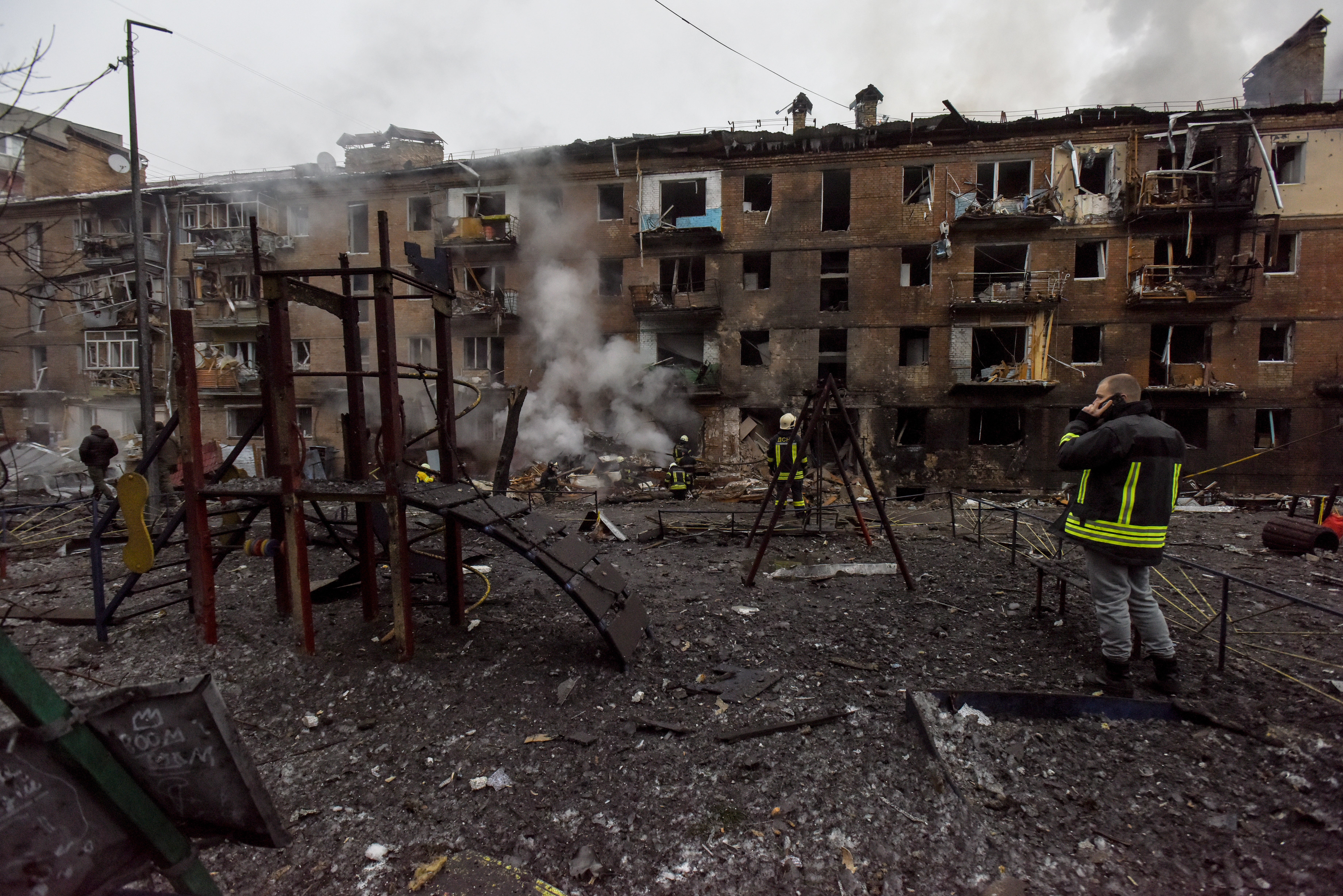 A destroyed children's playground as firefighters (rear) work at the site of an apartment block hit by shelling in Vyshhorod, near Kyiv