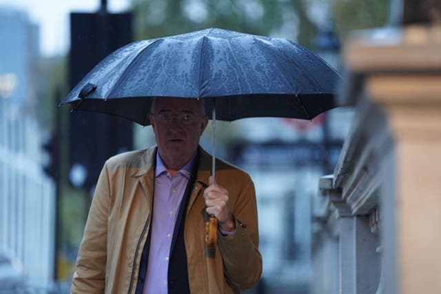 A man walks with an umbrella along Whitehall, London (PA)