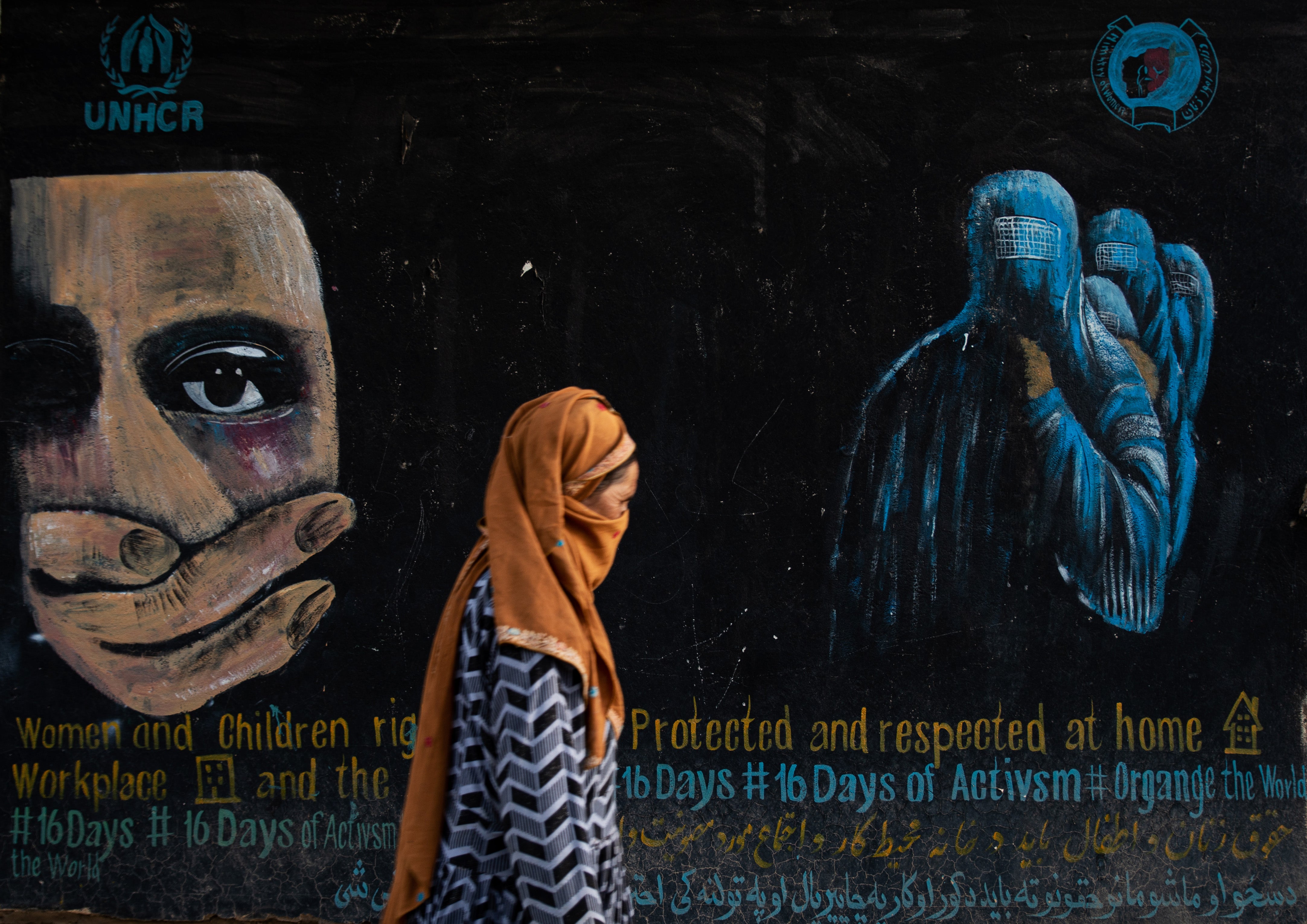 A woman walks past a mural calling for women and children’s rights in Afghanistan