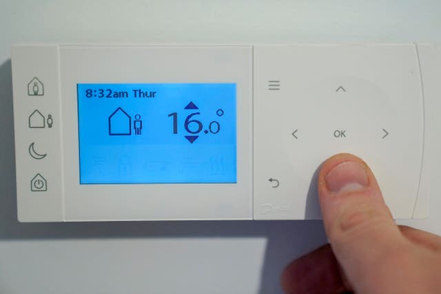 <p>A homeowner turning down the temperature on a central heating thermostat</p>