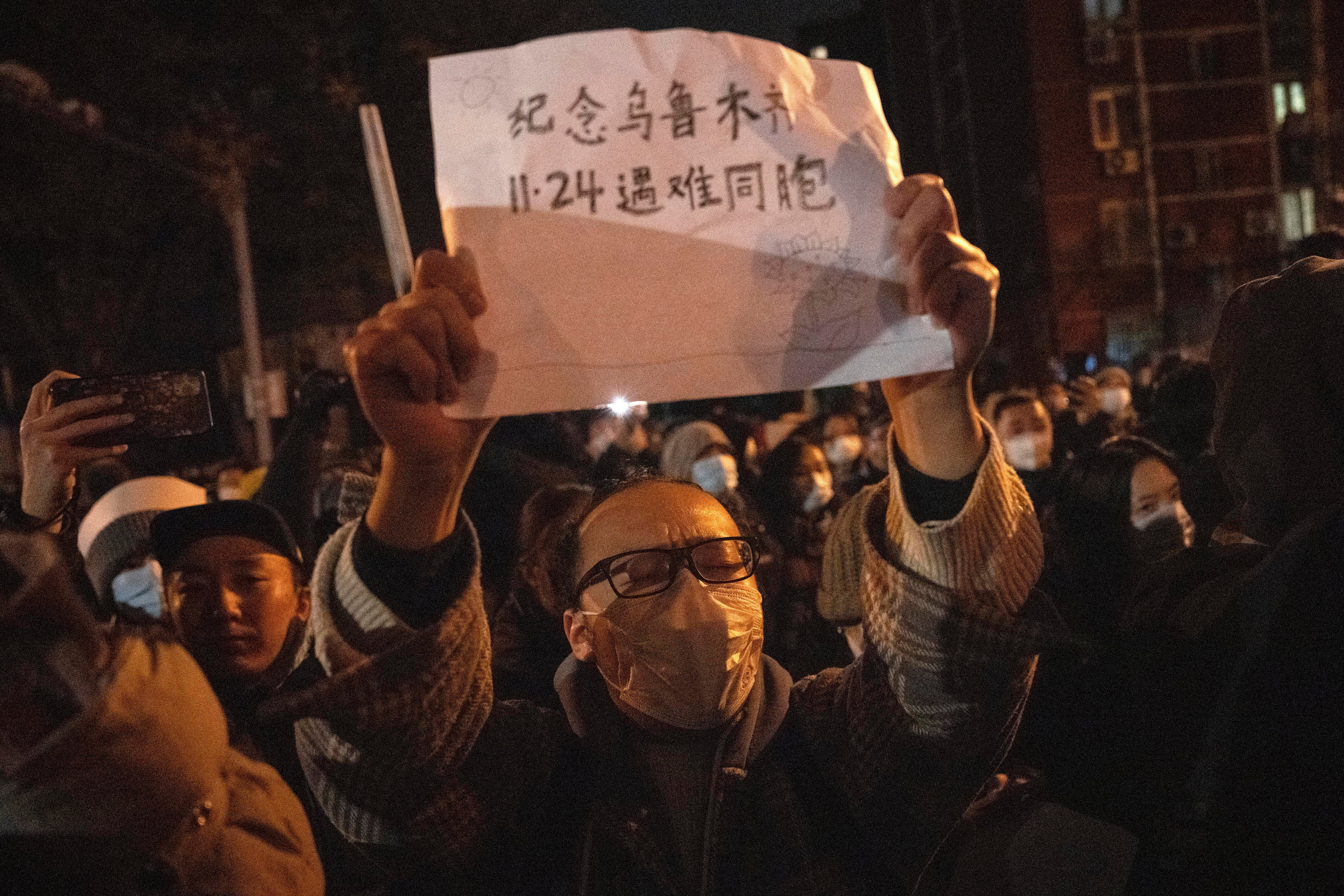 A protester holds up a sign which reads "Commemorate Urumqi Nov 24 compatriots who died" in Beijing