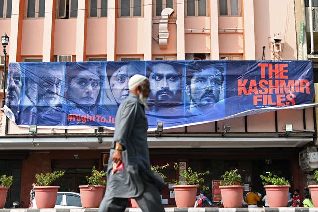 <p>A man walks past a banner of Bollywood movie ‘The Kashmir Files’ installed outside a cinema hall in the old quarters of Delhi on 21 March 2022</p>
