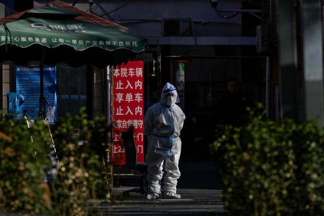 <p>A security guard in protective gear stands watch at an entrance gate to a neighborhood in Beijing</p>
