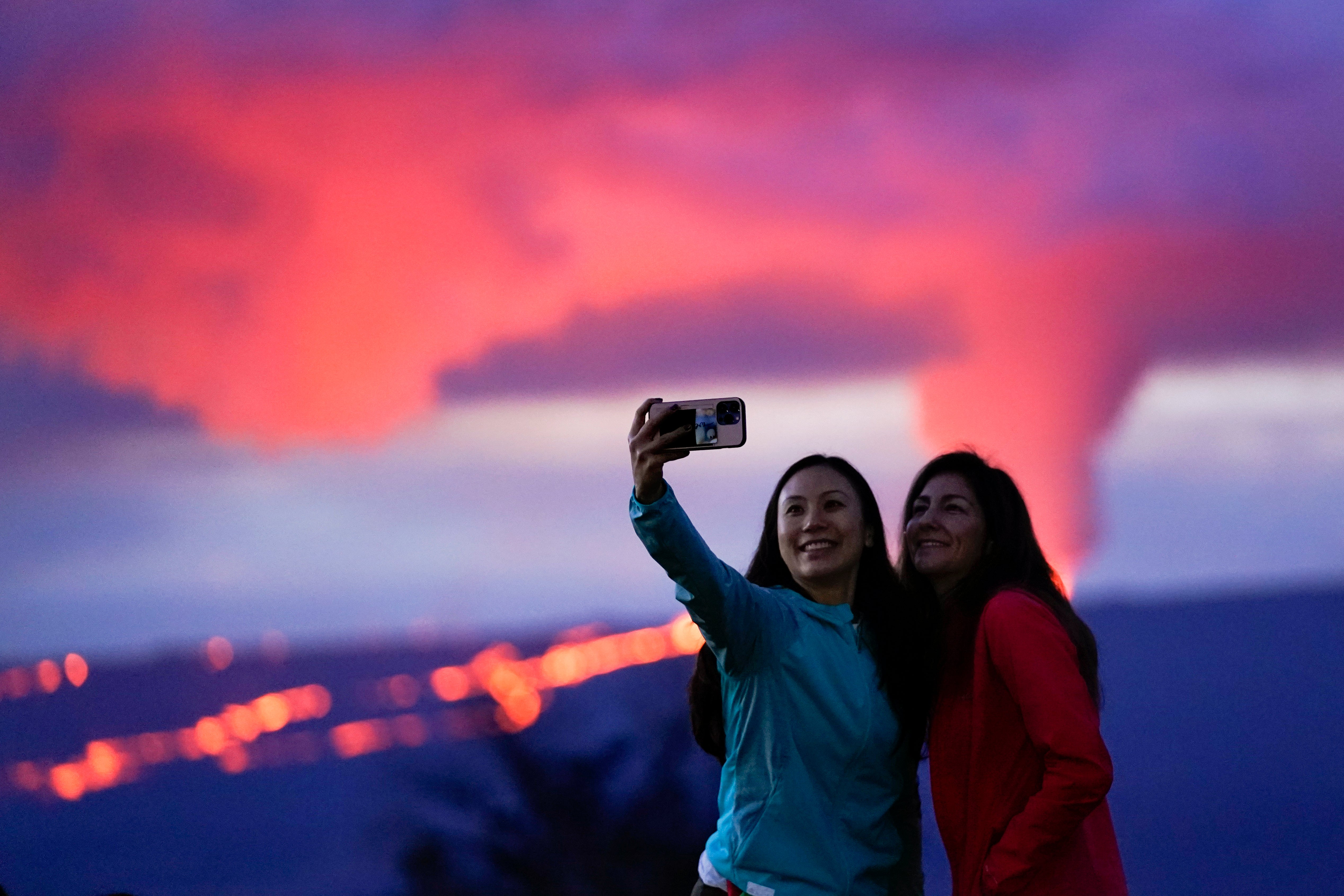 Ingrid Yang, left, and Kelly Bruno, both of San Diego, take a photo in front of lava erupting from Hawaii's Mauna Loa volcano Wednesday, Nov. 30, 2022, near Hilo, Hawaii